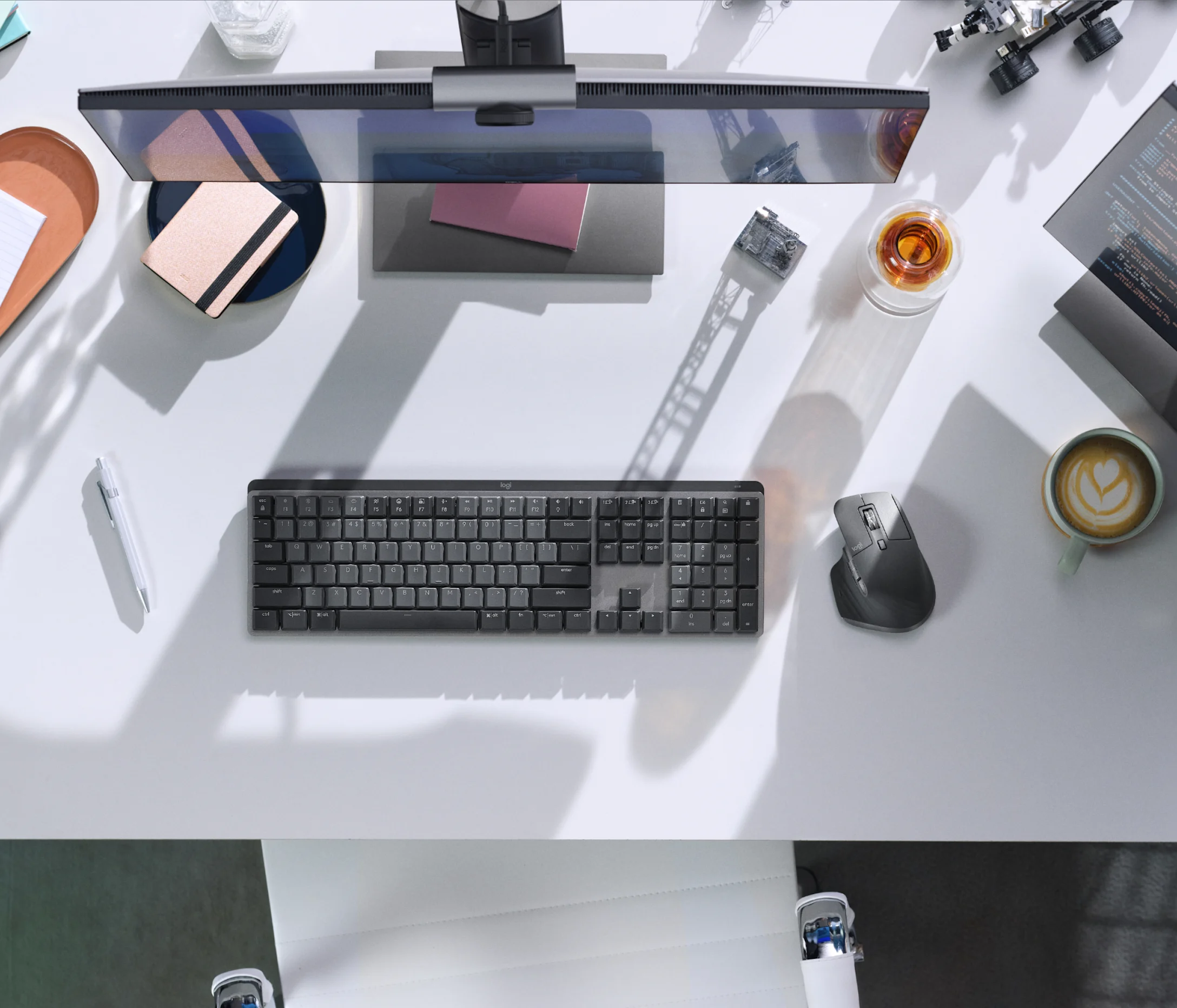 Vista dall'alto di una scrivania moderna con monitor, tastiera, mouse, taccuino, tazza di caffè e vari accessori.