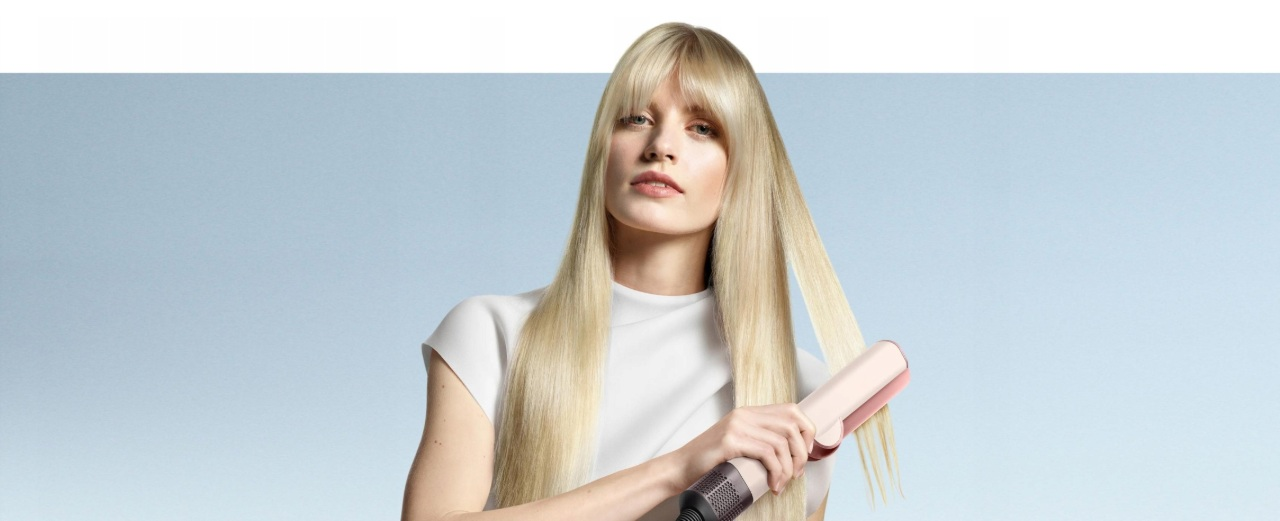 Blond kobieta z prostymi wlosami używająca różowej prostownicy na niebieskim tle.