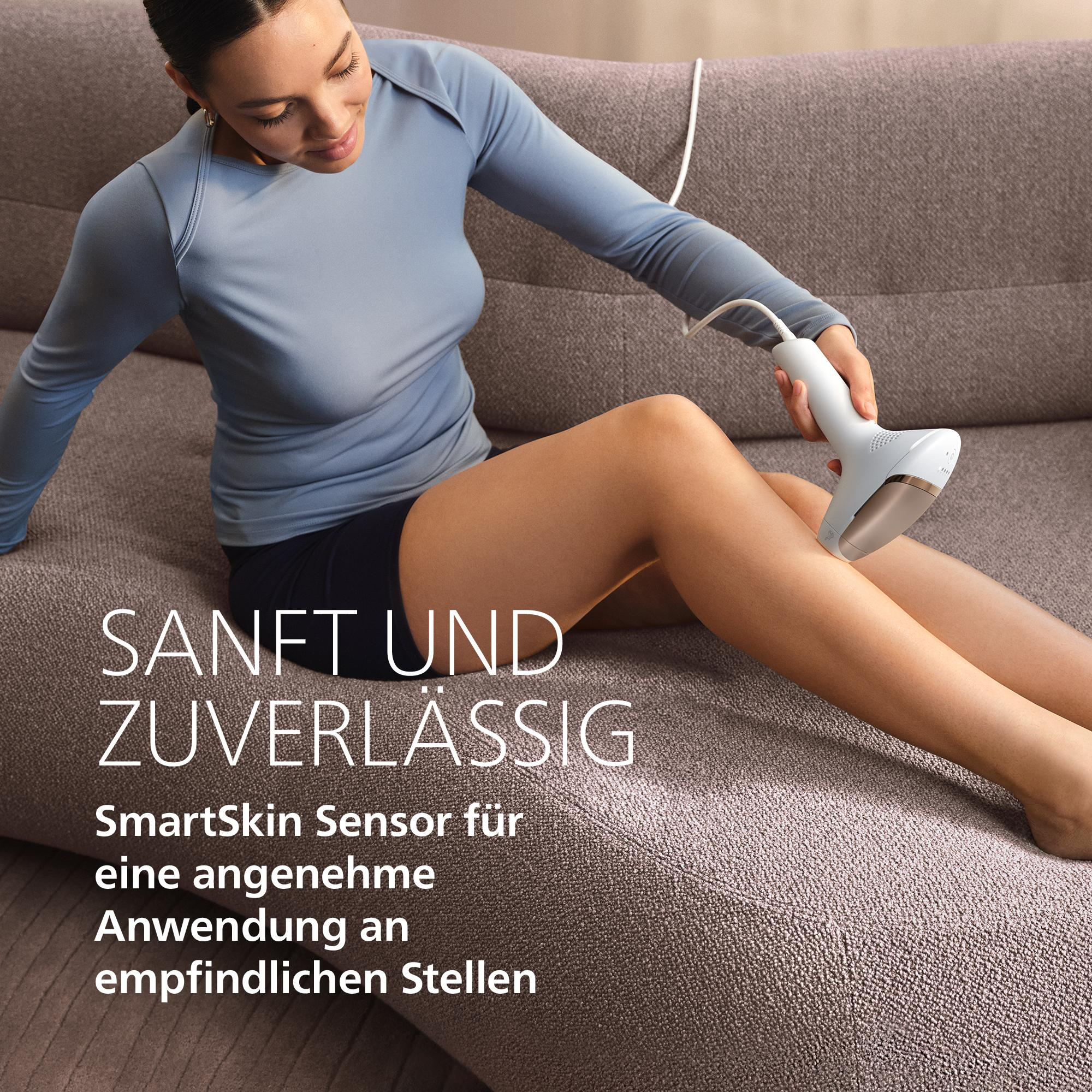 Eine Frau sitzt auf einem Sofa und verwendet ein weißes IPL-Gerät an ihrem Bein.