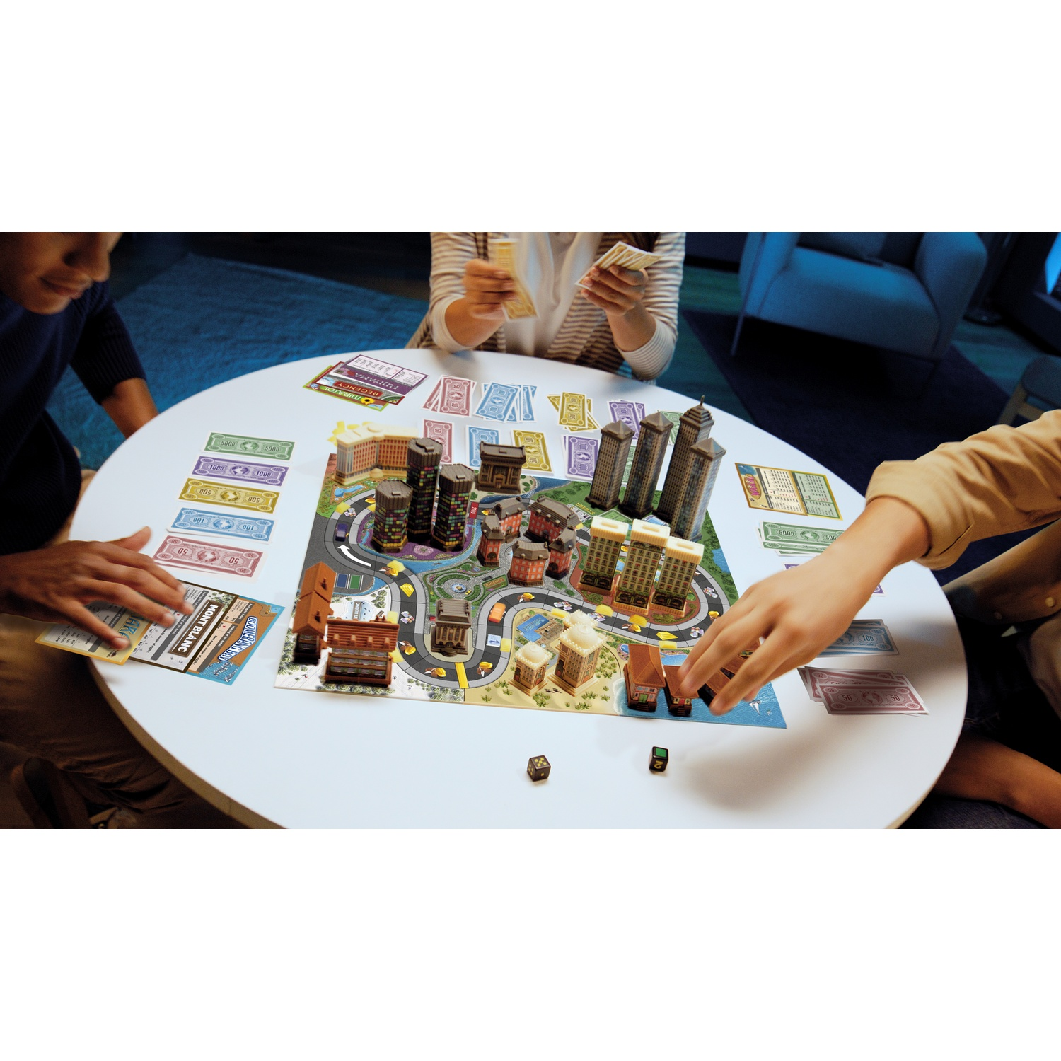 Three people playing a Monopoly board game with 3D buildings on a round table.