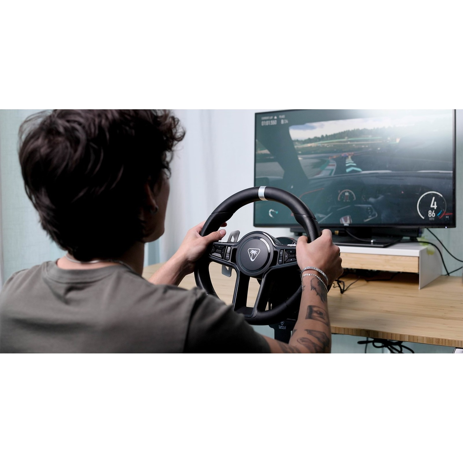 A young man sits in front of a monitor playing a racing game with a steering wheel.