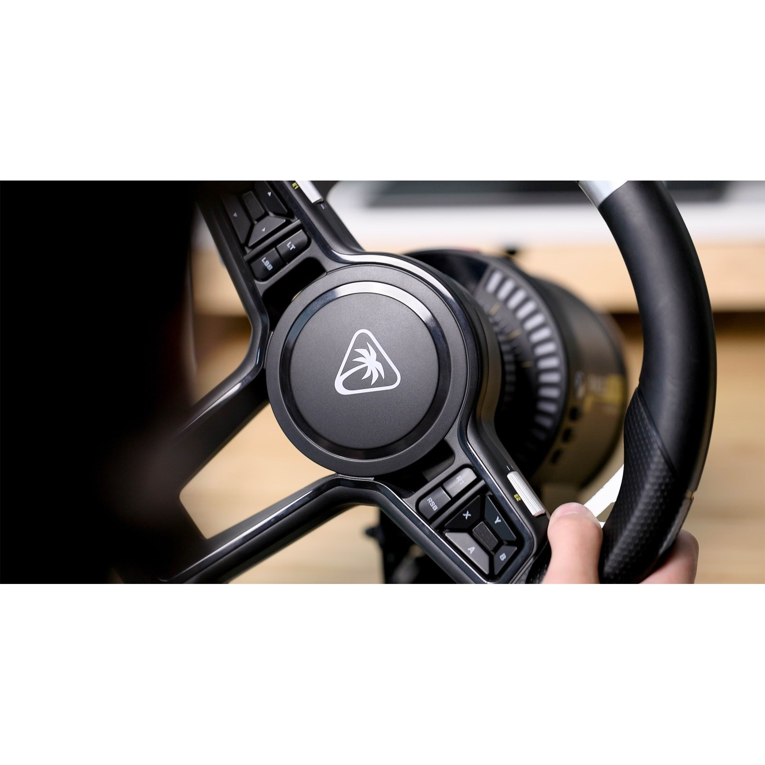 A black sim-racing steering wheel with a central logo and integrated buttons is held by a hand.
