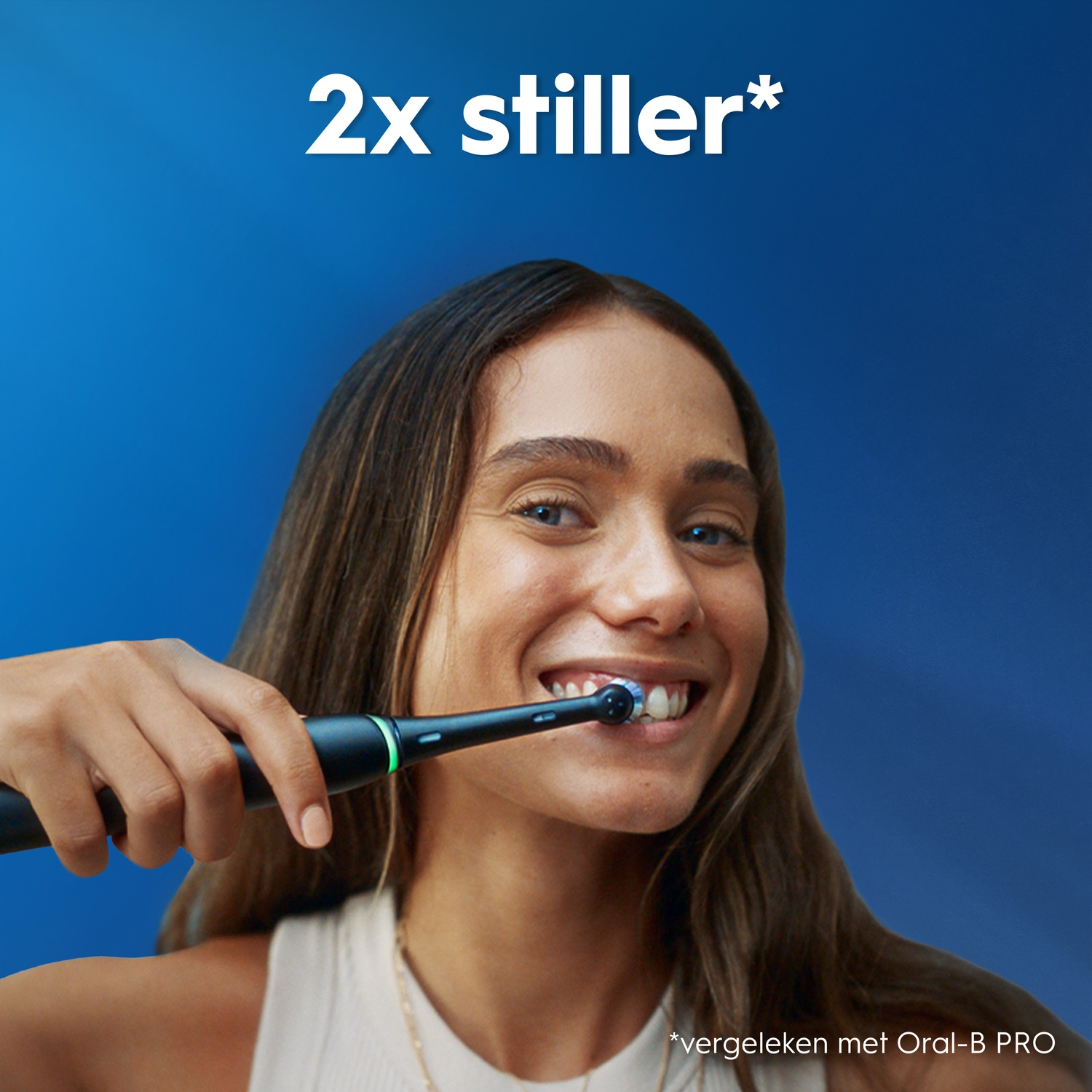 A young woman smiling while brushing her teeth with a black electric toothbrush against a blue background.