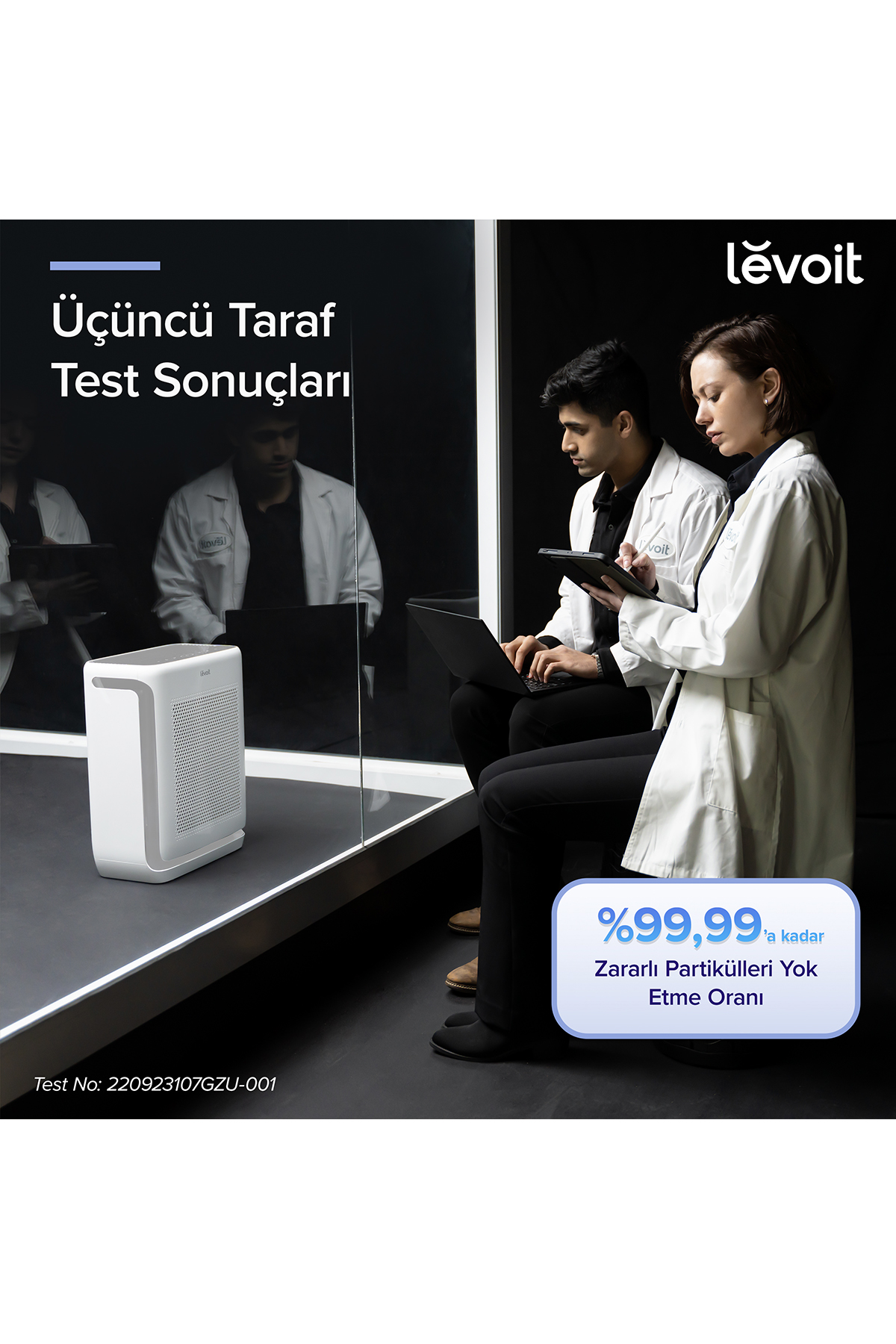 Laboratuvar önlüklü iki araştırmacı, beyaz bir hava temizleyicinin yanında modern bir odada çalışıyor.