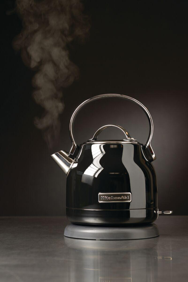 Ein schwarzer KitchenAid-Wasserkocher steht auf einer Basis und stößt Dampf aus.