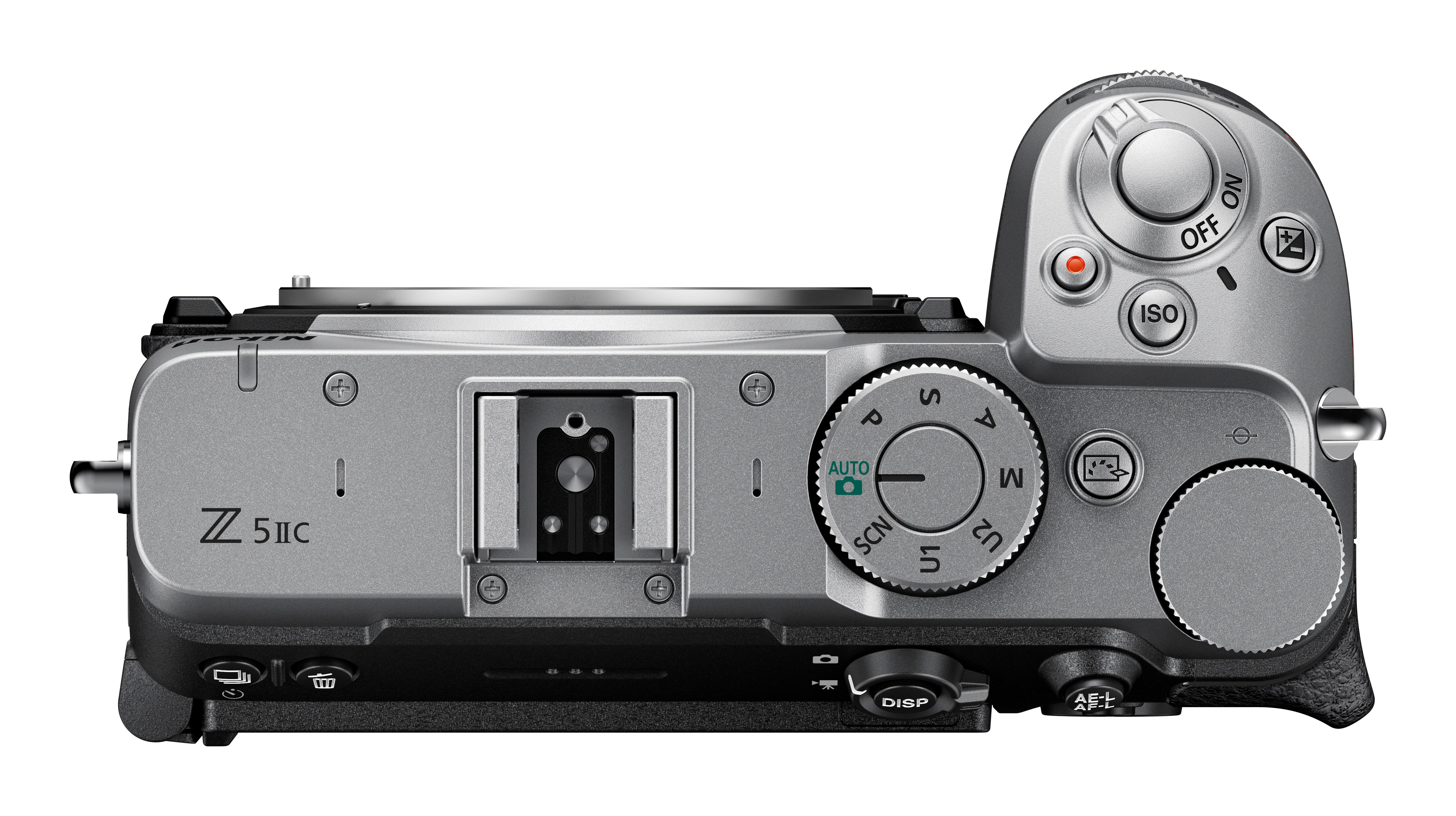 Draufsicht einer silbernen Nikon Z f Kamera mit Einstellrädern, Tasten und Blitzschuh vor weißem Hintergrund.