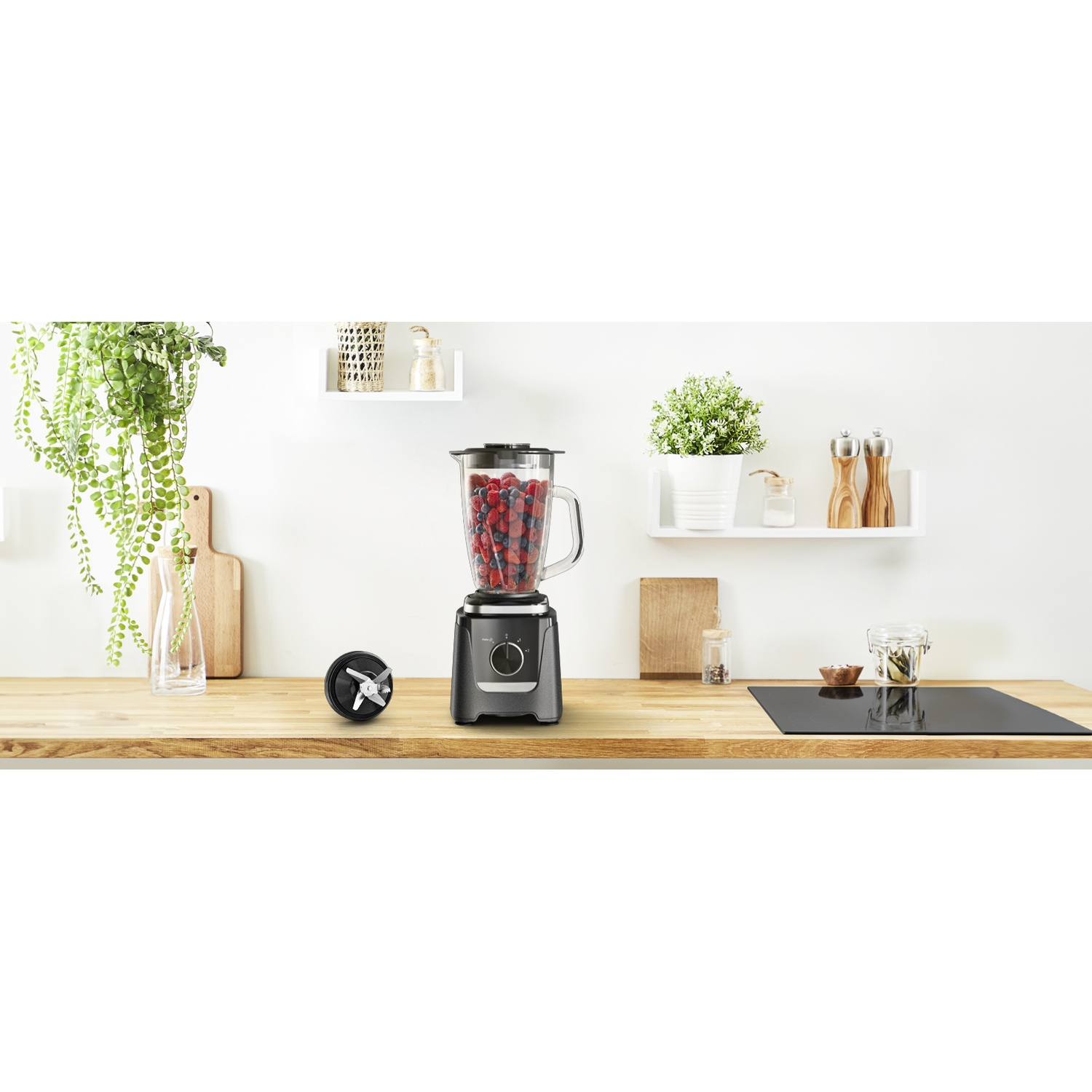 Un blender noir rempli de baies rouges et de myrtilles repose sur un comptoir en bois, avec une lame à côté.
