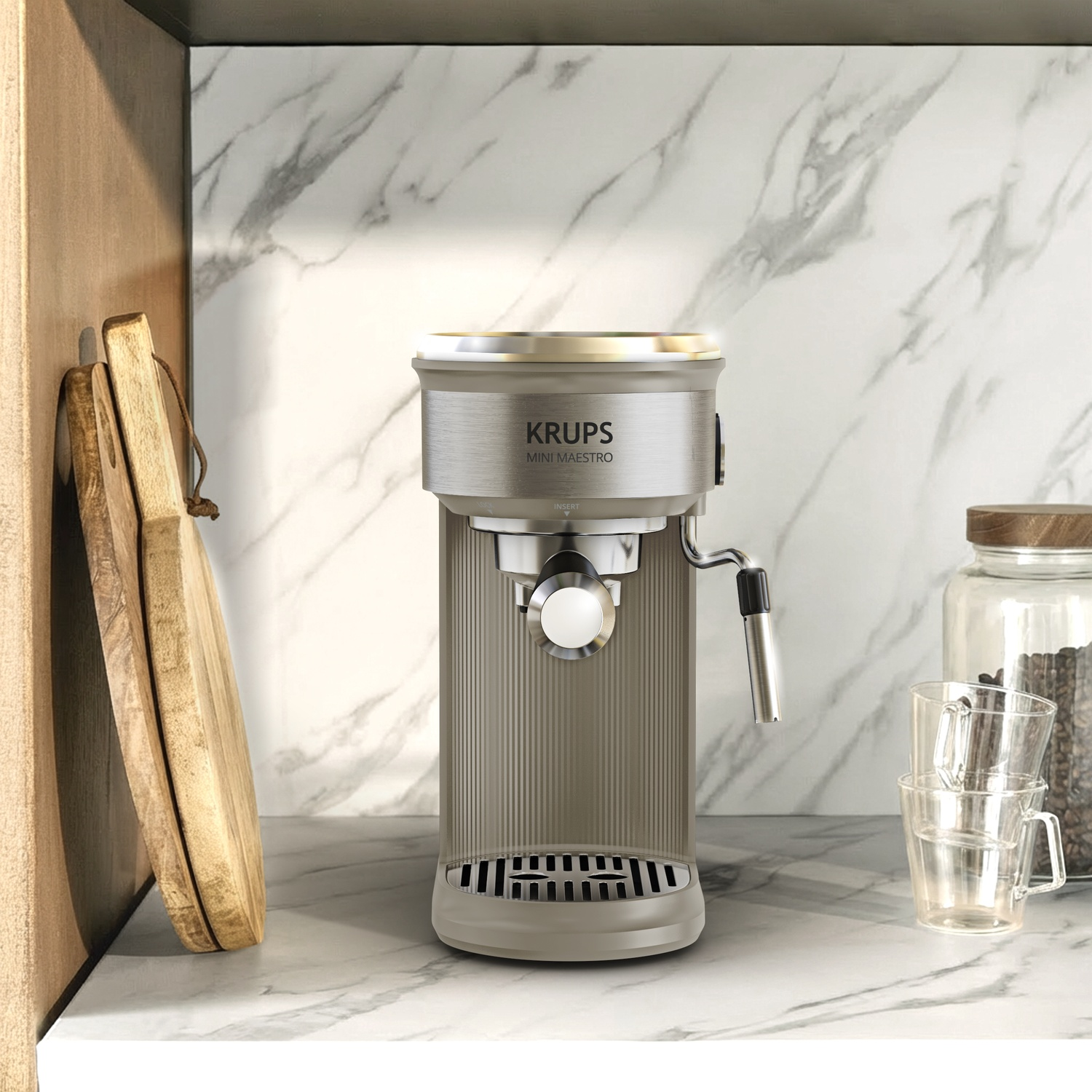Krups Mini Maestro koffiemachine op een marmeren aanrecht met houten planken en glazen.