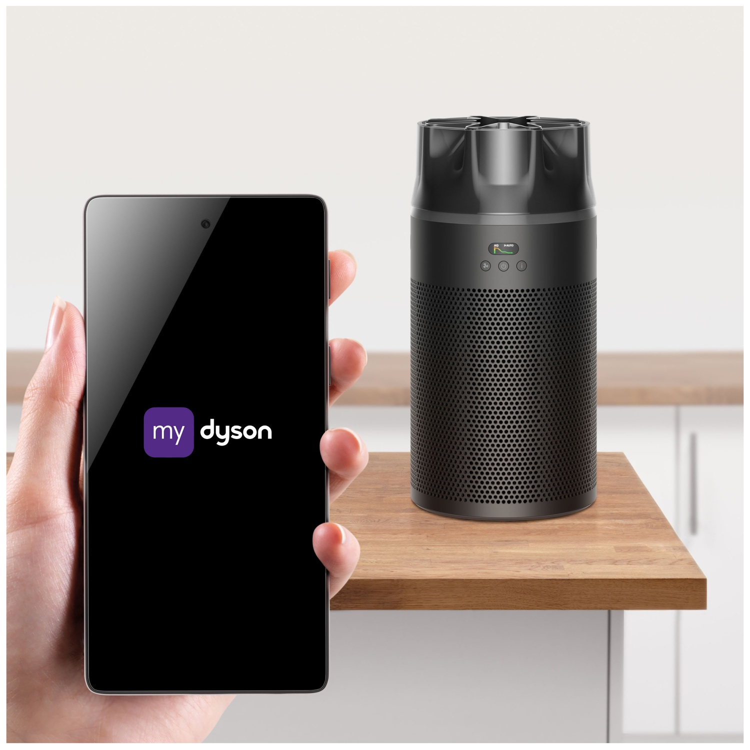 Une main tient un smartphone affichant l'application MyDyson, à côté d'un purificateur d'air noir sur une table en bois.