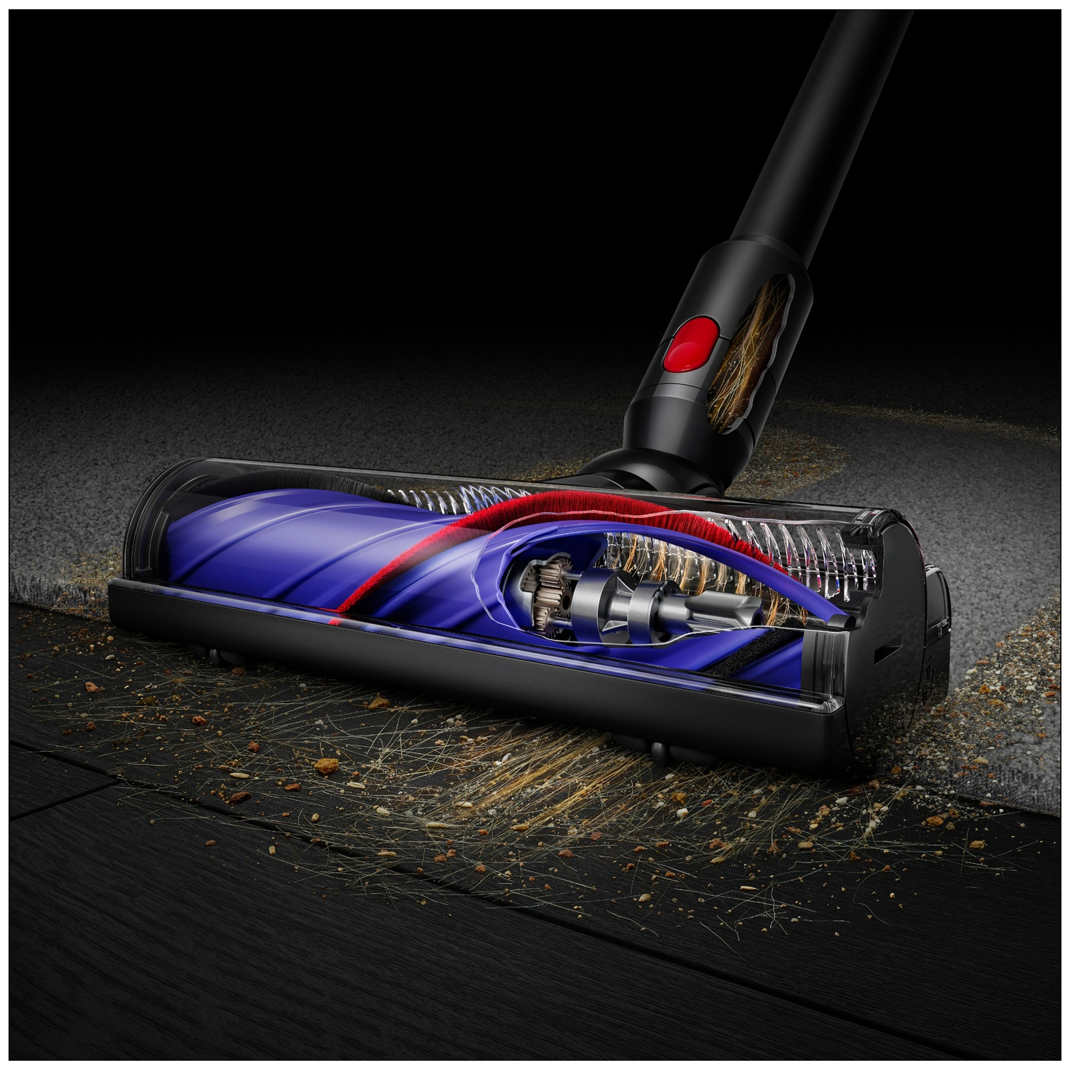 Vacuum cleaner head with blue and red brush on carpet and dark floor, picking up hair and debris.