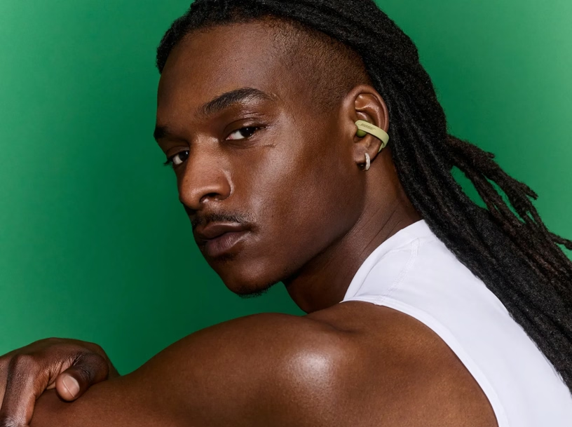 Ein Mann mit Dreadlocks und grünem Ohrhörer vor grünem Hintergrund.
