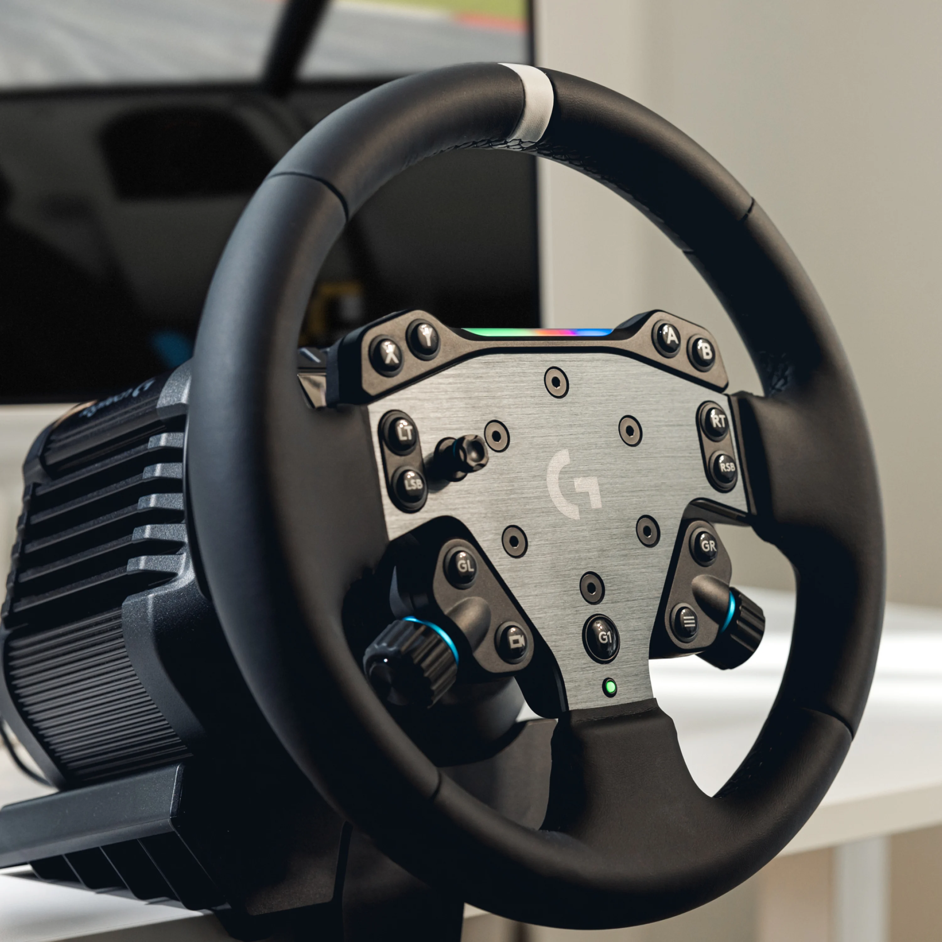 Schwarzes Logitech-Rennlenkrad mit silberner Frontplatte und zahlreichen Bedientasten vor einem Bildschirm.