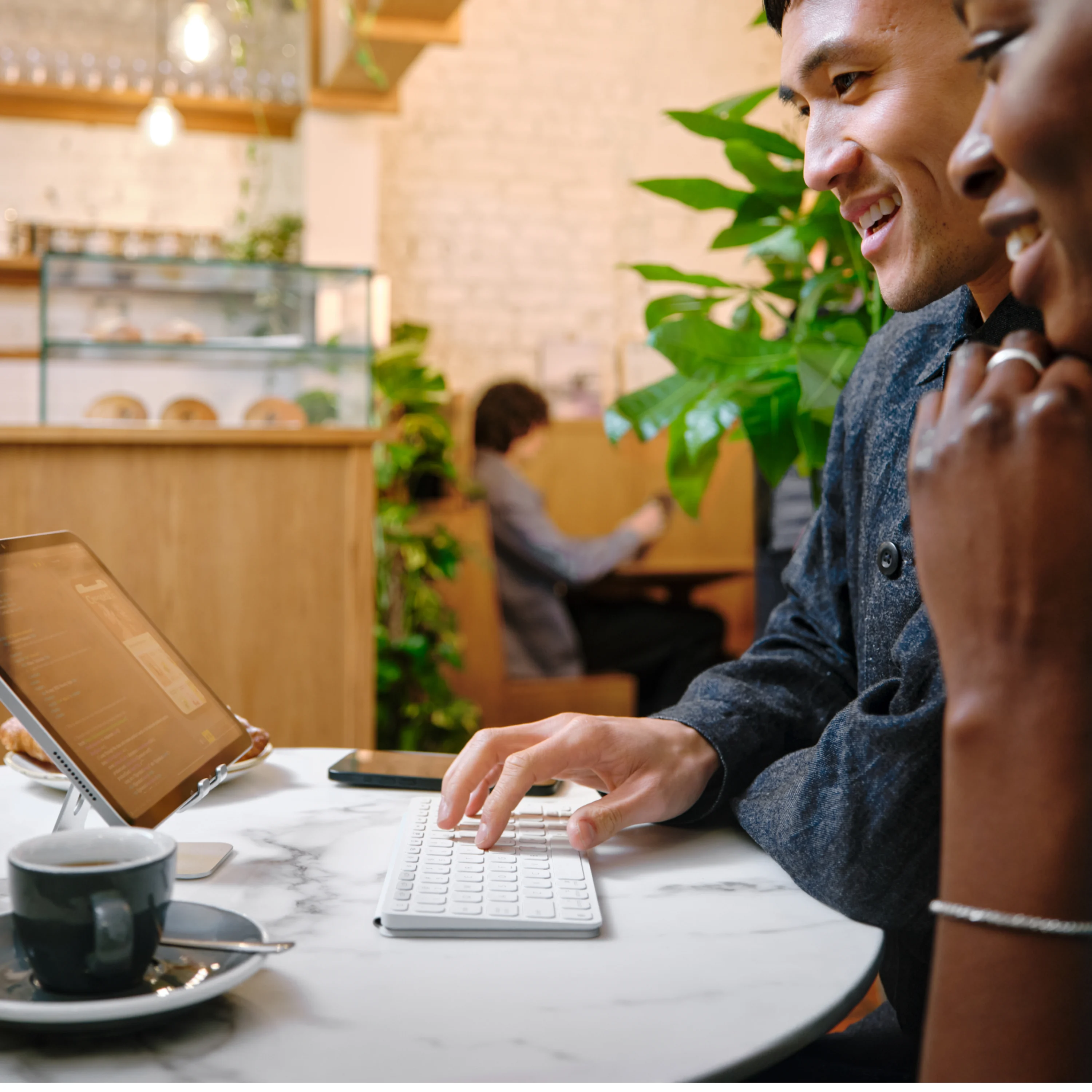 Uomo e donna sorridono mentre lui digita su una tastiera in un caffè.