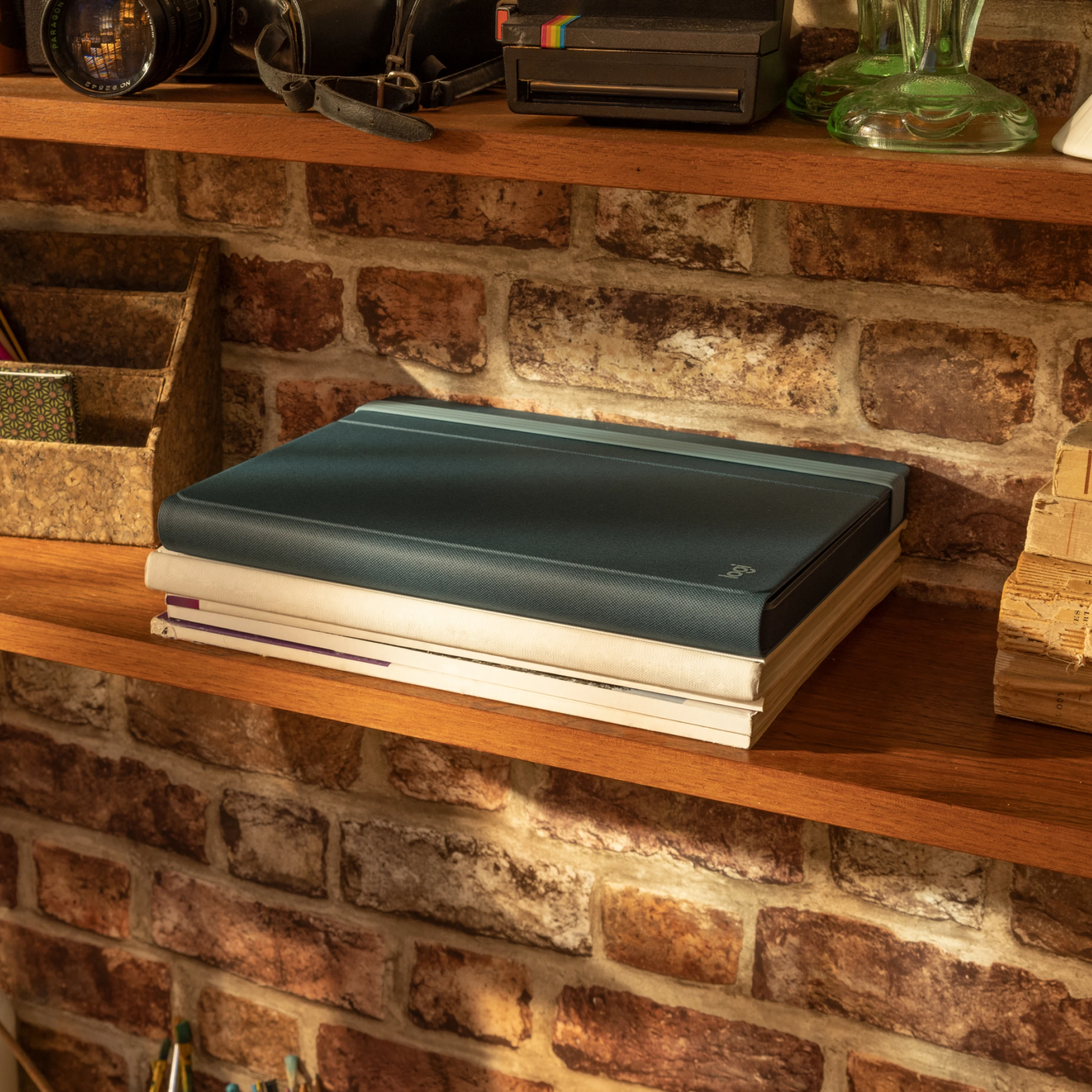 Un tablet blu scuro chiuso in una custodia poggia su dei libri su un ripiano di legno davanti a un muro di mattoni.