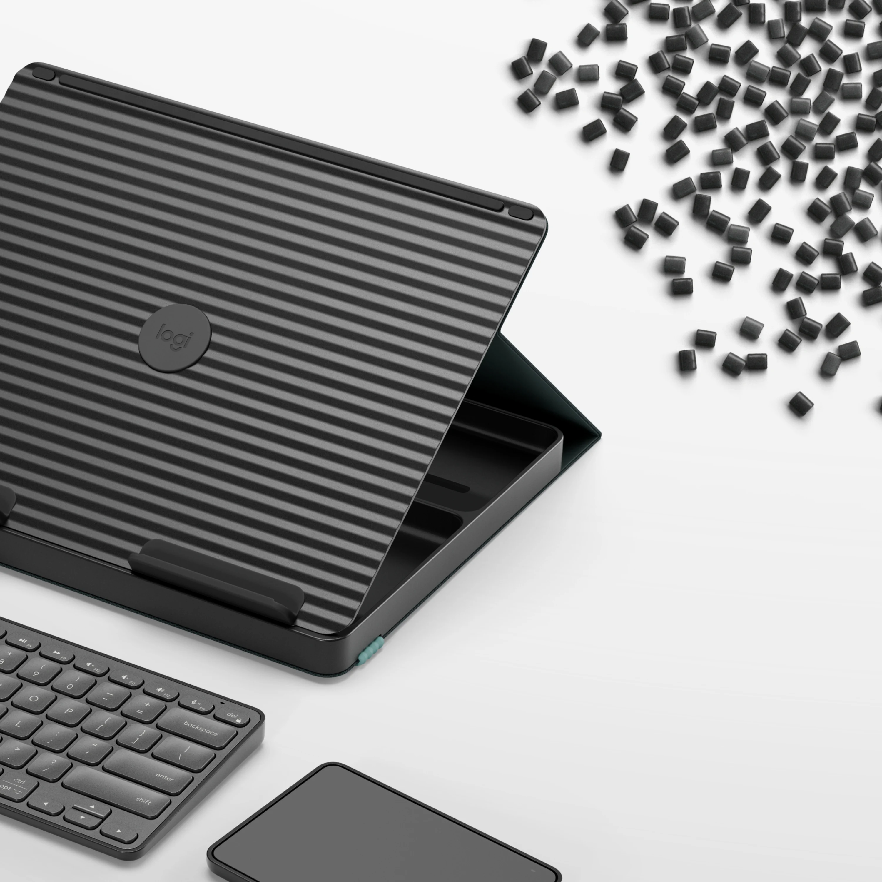 Custodia per tablet Logitech nera a coste, una tastiera e piccoli pellet di plastica su sfondo bianco.