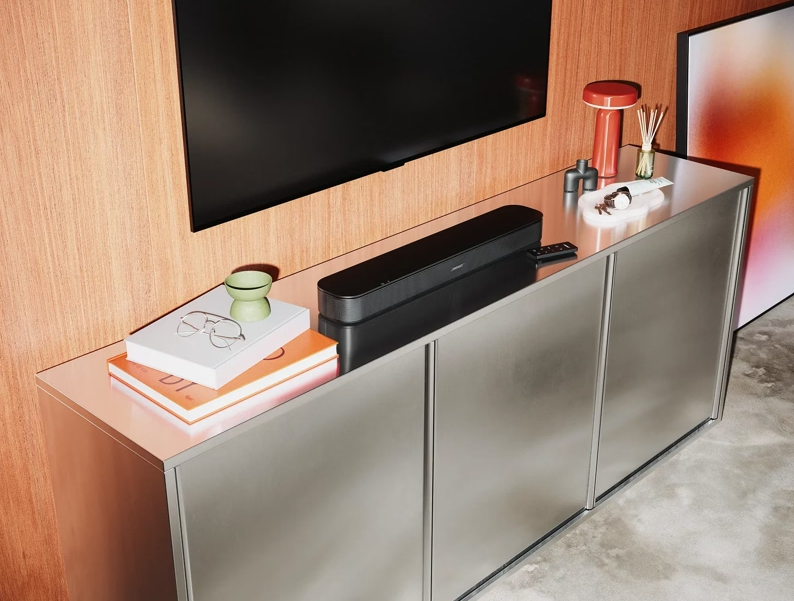 Soundbar na metalowej komodzie pod telewizorem, z książkami i ozdobami.
