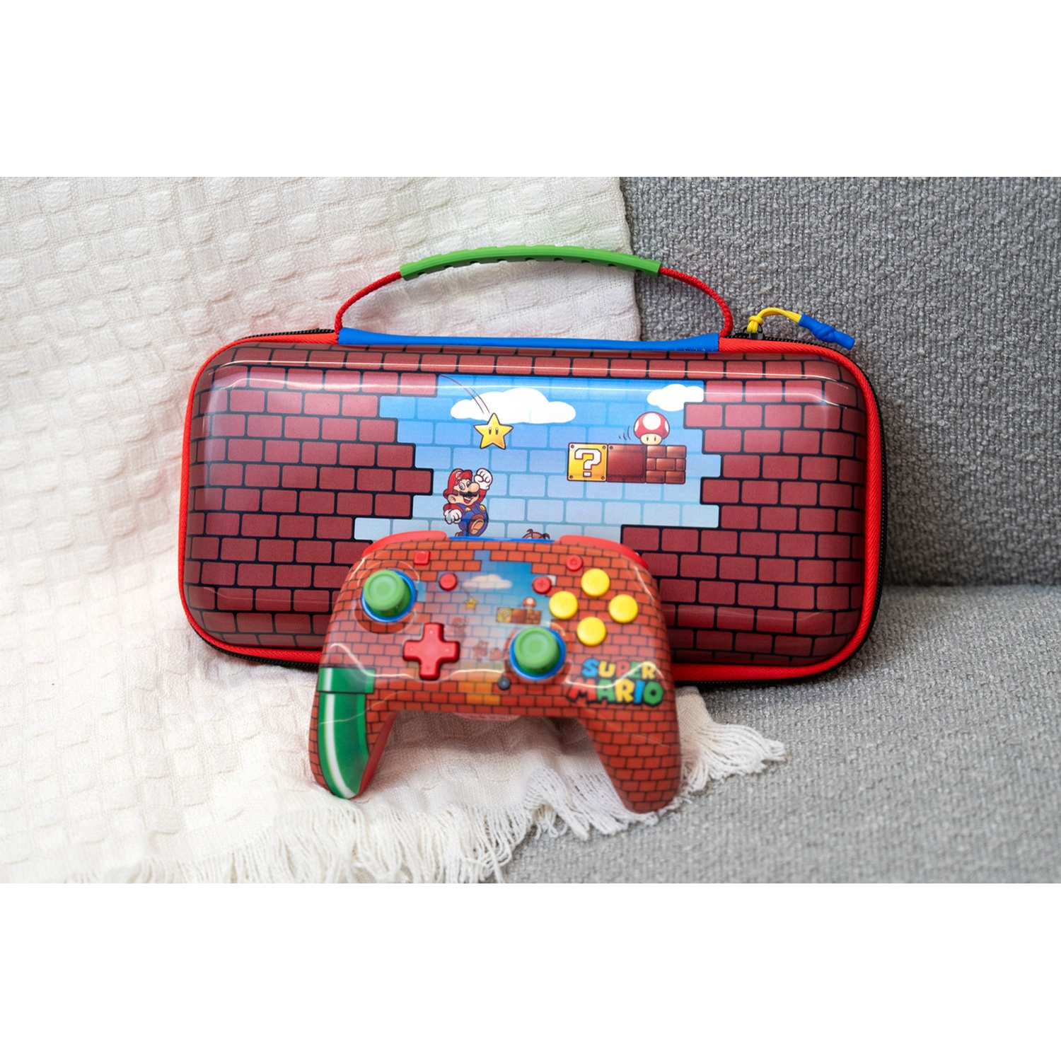 A Super Mario themed carrying case and matching game controller on a gray couch.