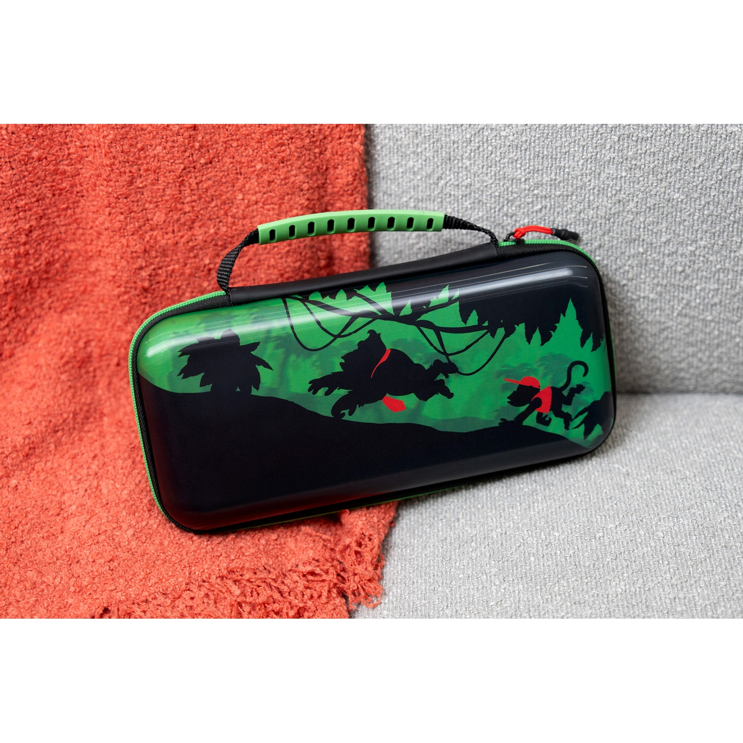 A black and green gaming case with a jungle design sits on an orange and grey blanket.