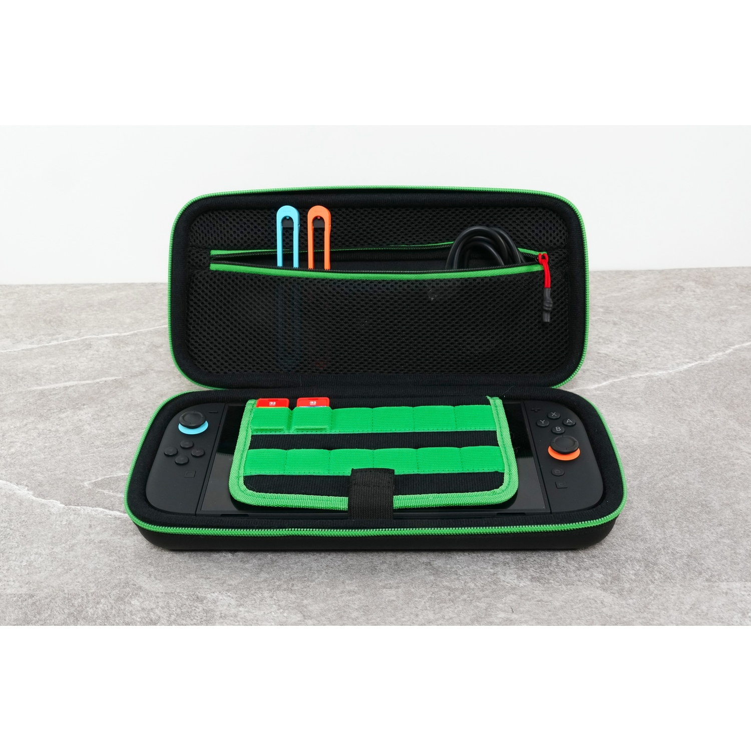 An open black case with green trim contains a console, blue and orange joy-cons, and accessories.