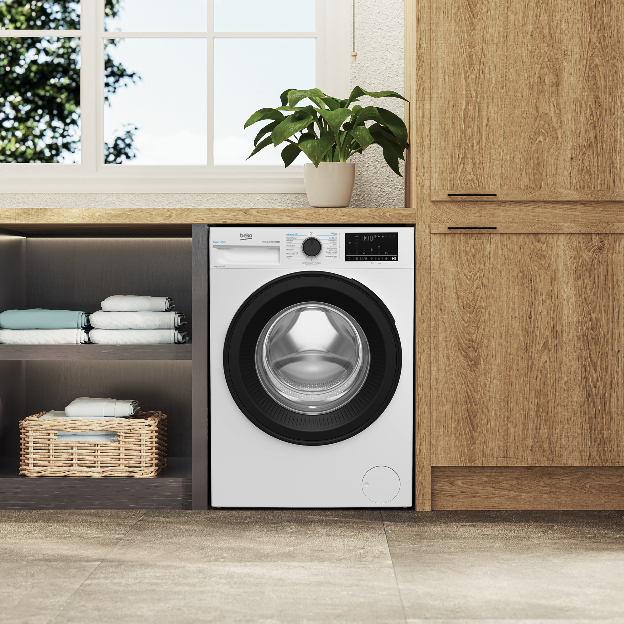 A white washing machine in a modern kitchen with wooden cabinets, folded towels on shelves, and a potted plant.