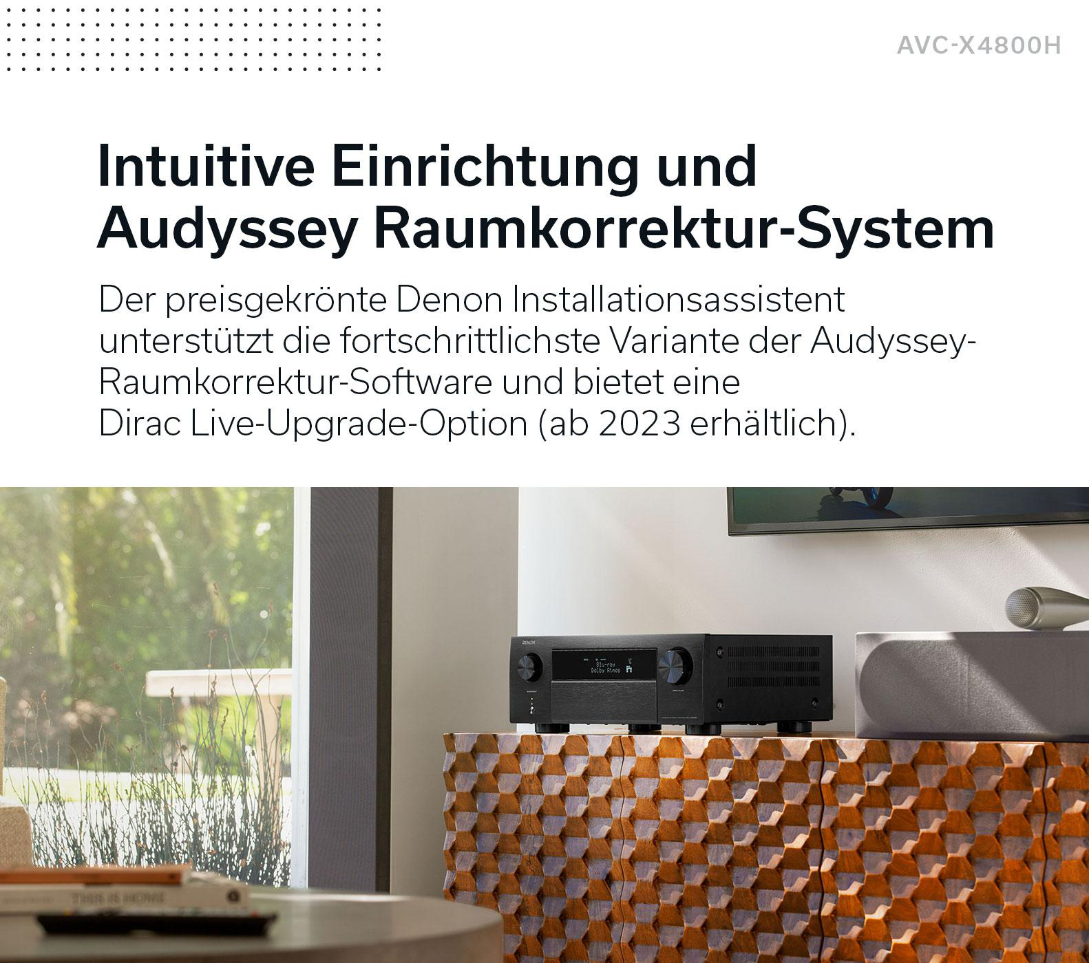 Ein Denon AV-Receiver steht auf einer gemusterten Holzkommode in einem modernen Raum mit Text auf Deutsch.