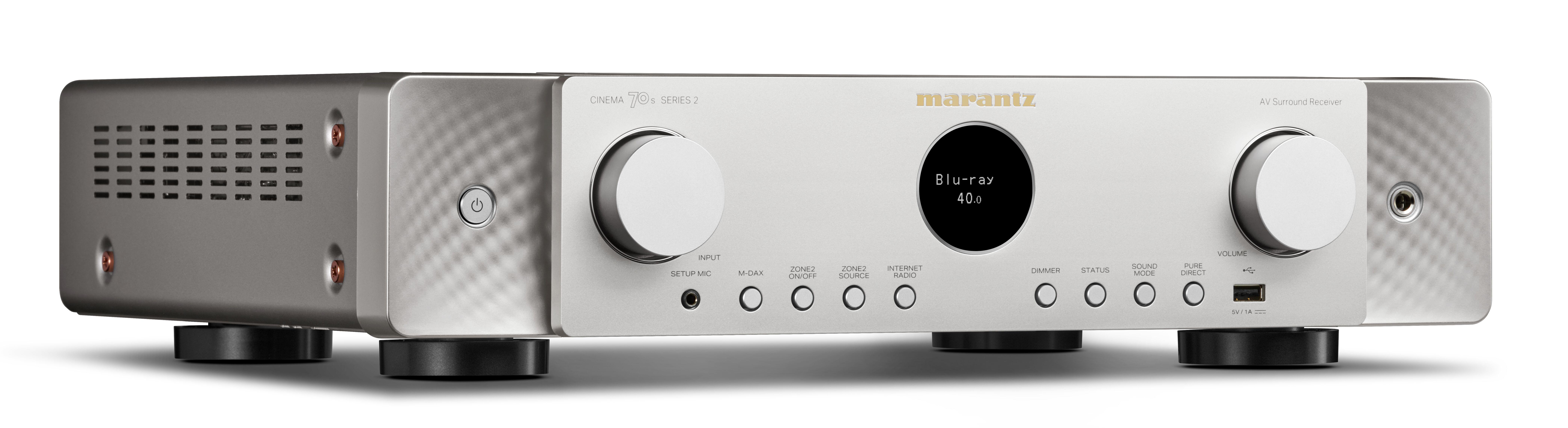 Silberner Marantz AV-Surround-Receiver mit zentralem Display, Drehreglern und Tasten auf einer weißen Oberfläche.