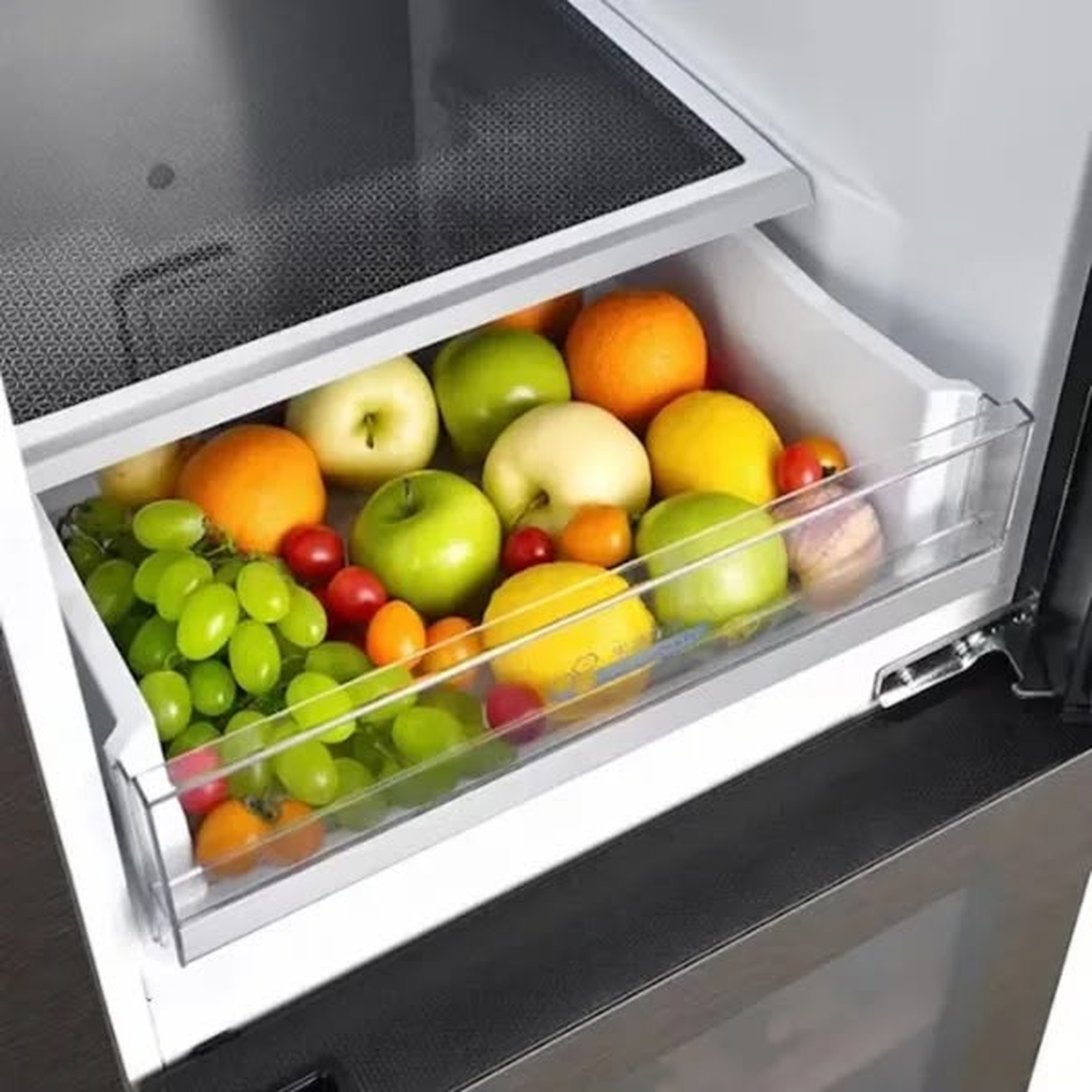 Un cassetto per verdure del frigorifero aperto pieno di frutta fresca come mele, arance e uva.