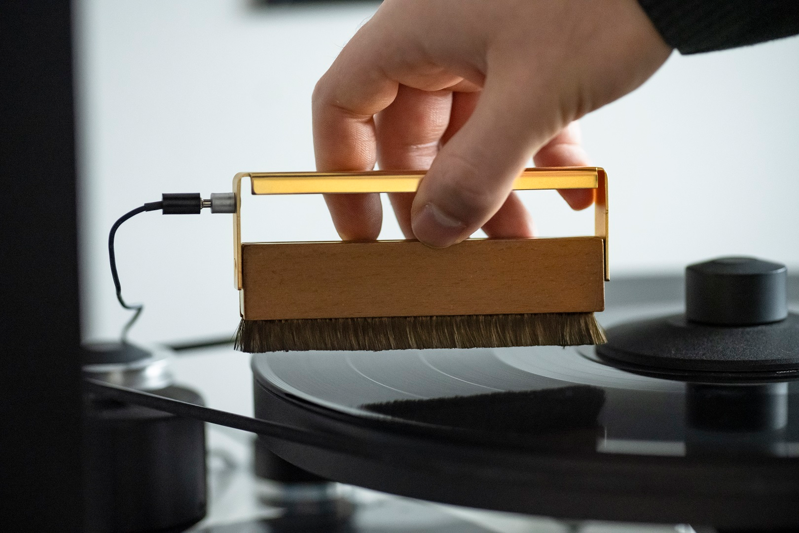 Eine Hand reinigt eine Vinylplatte auf einem Plattenspieler mit einer goldenen Bürste.