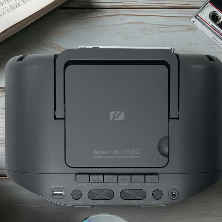 Vue de dessus d'un lecteur cassette radio CD portable gris foncé sur une table en bois avec une cassette et des partitions.