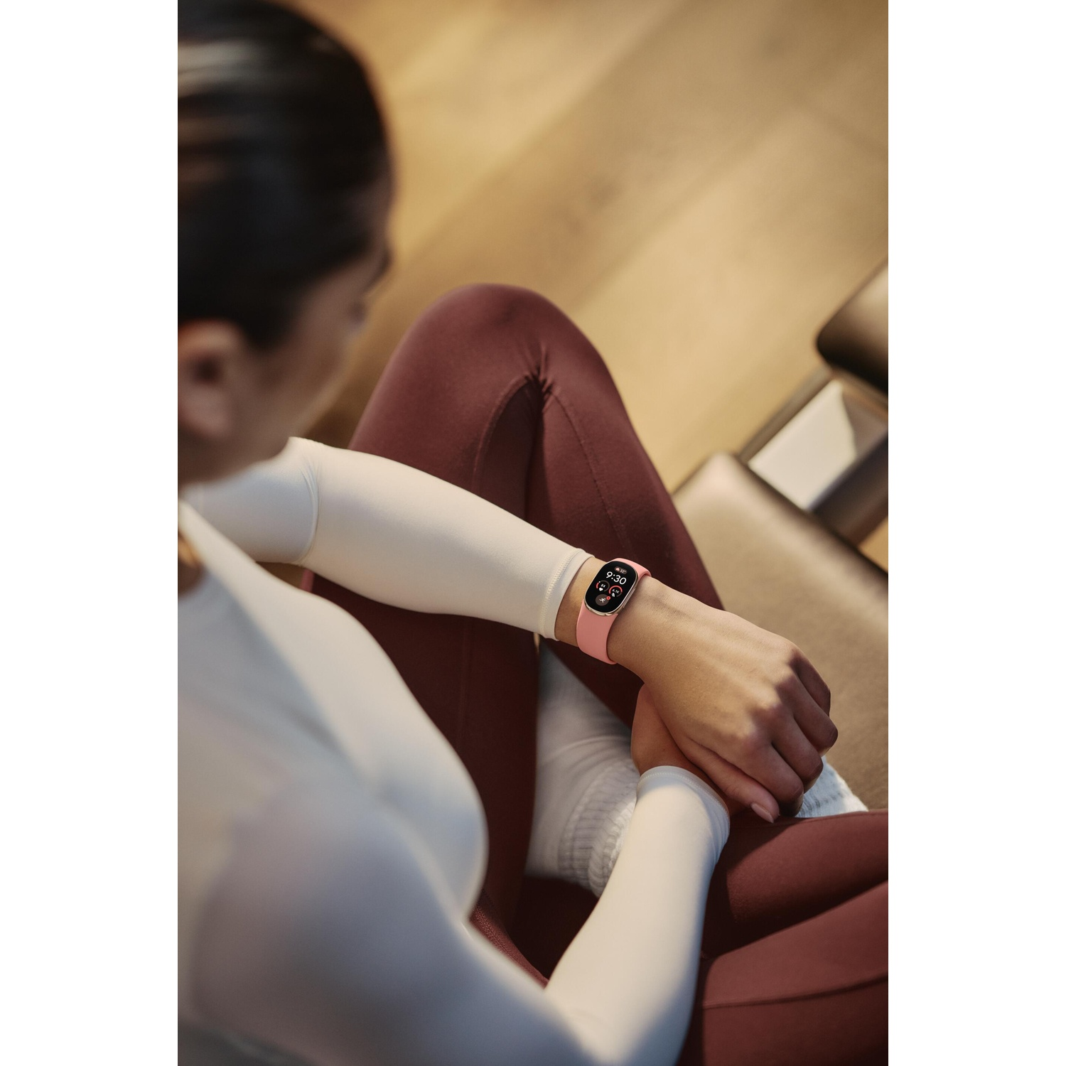 Vrouw in sportkleding zit in kleermakerszit met een roze smartwatch om haar pols.