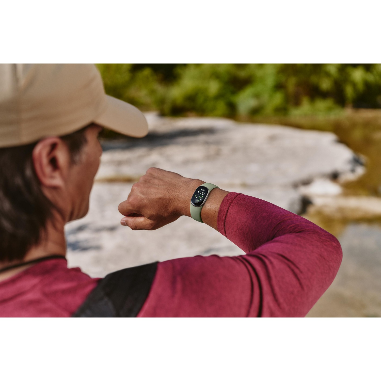 Een man met een pet en rode truien kijkt naar zijn groen smartwatch buiten.
