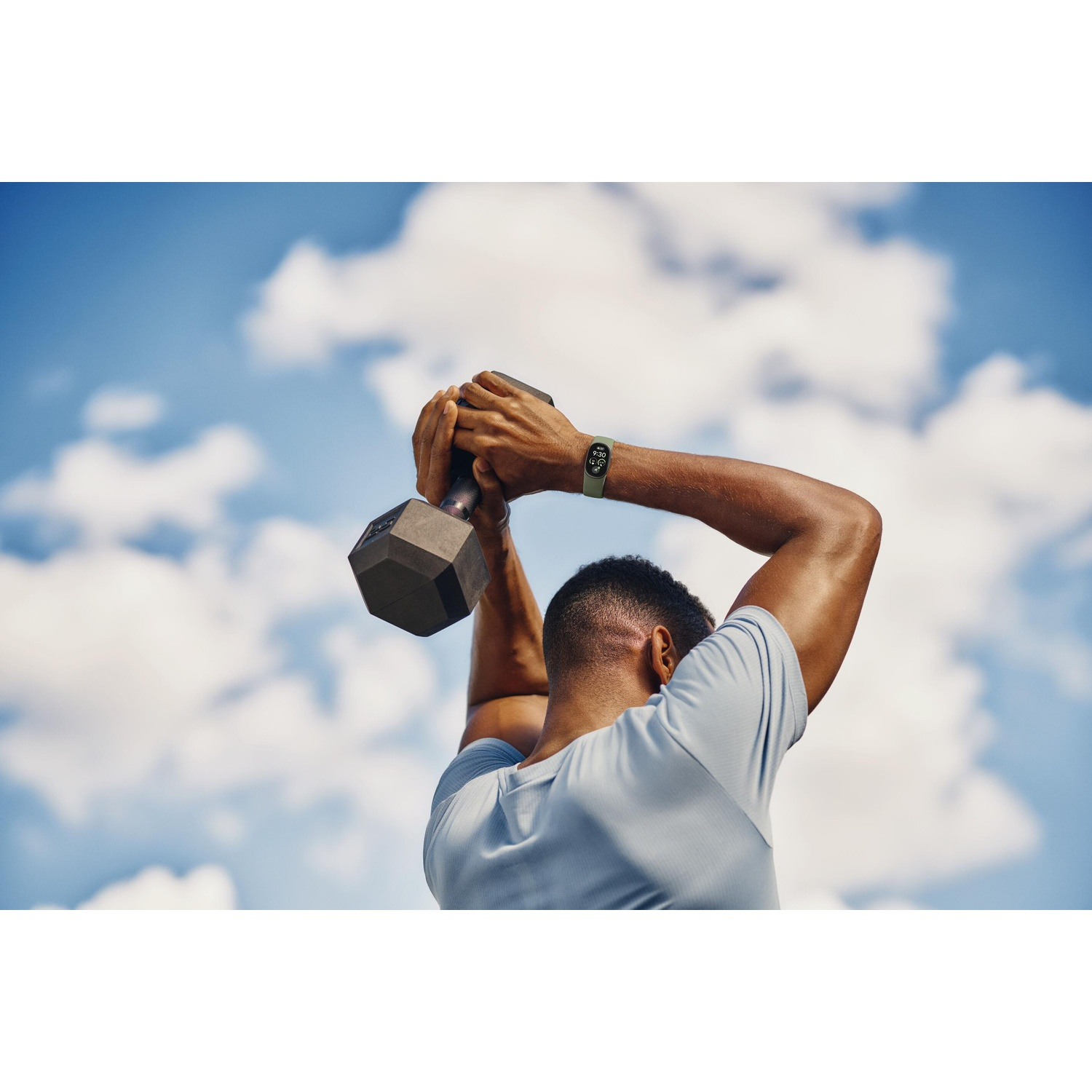 Een man in een blauw shirt tilt een dumbbell op tegen een bewolkte blauwe hemel.
