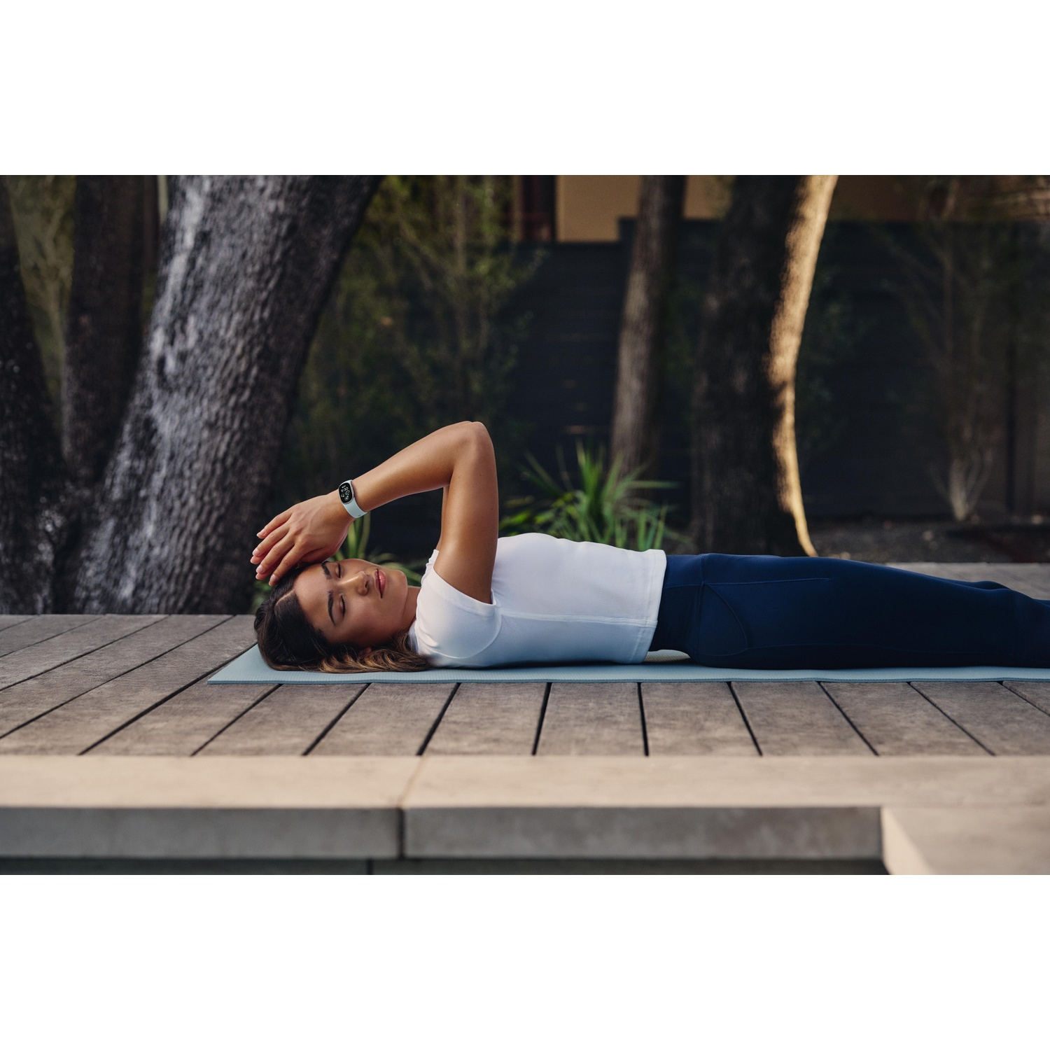Een vrouw ligt op een yogamat op een houten terras buiten.
