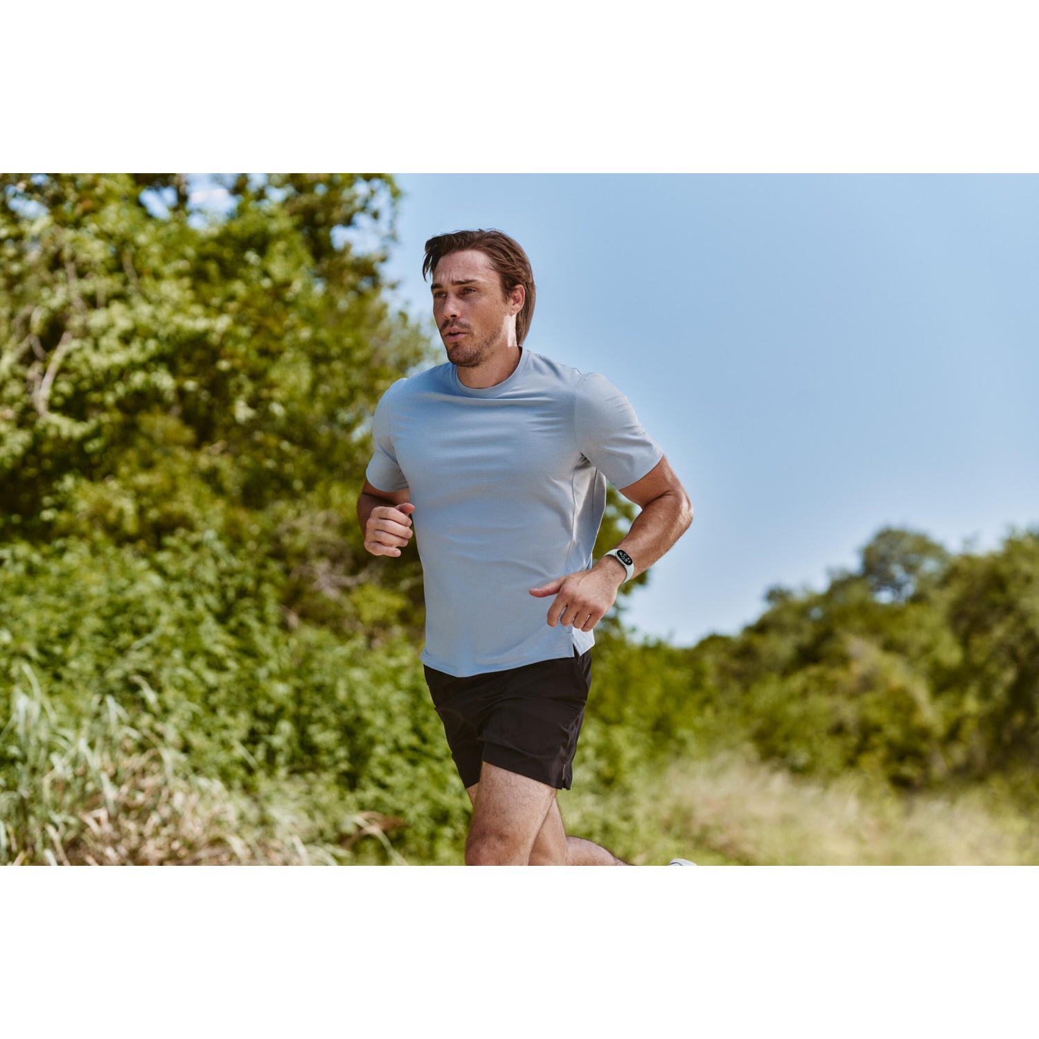 Een man in een blauw t-shirt hardloopt buiten met groene bomen en blauwe lucht.
