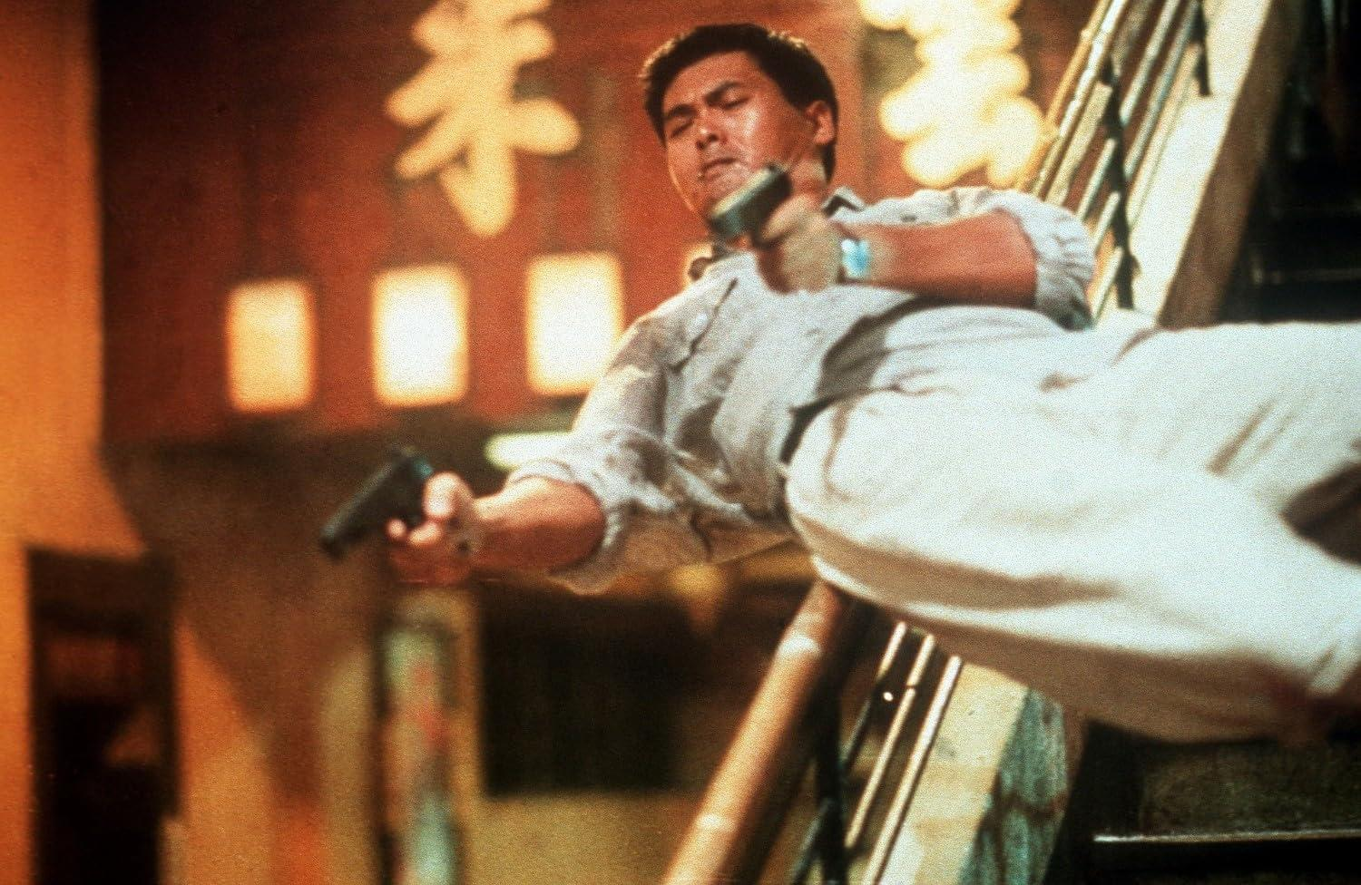 Ein Mann im hellen Anzug gleitet eine Treppe herunter und hält in jeder Hand eine Waffe.