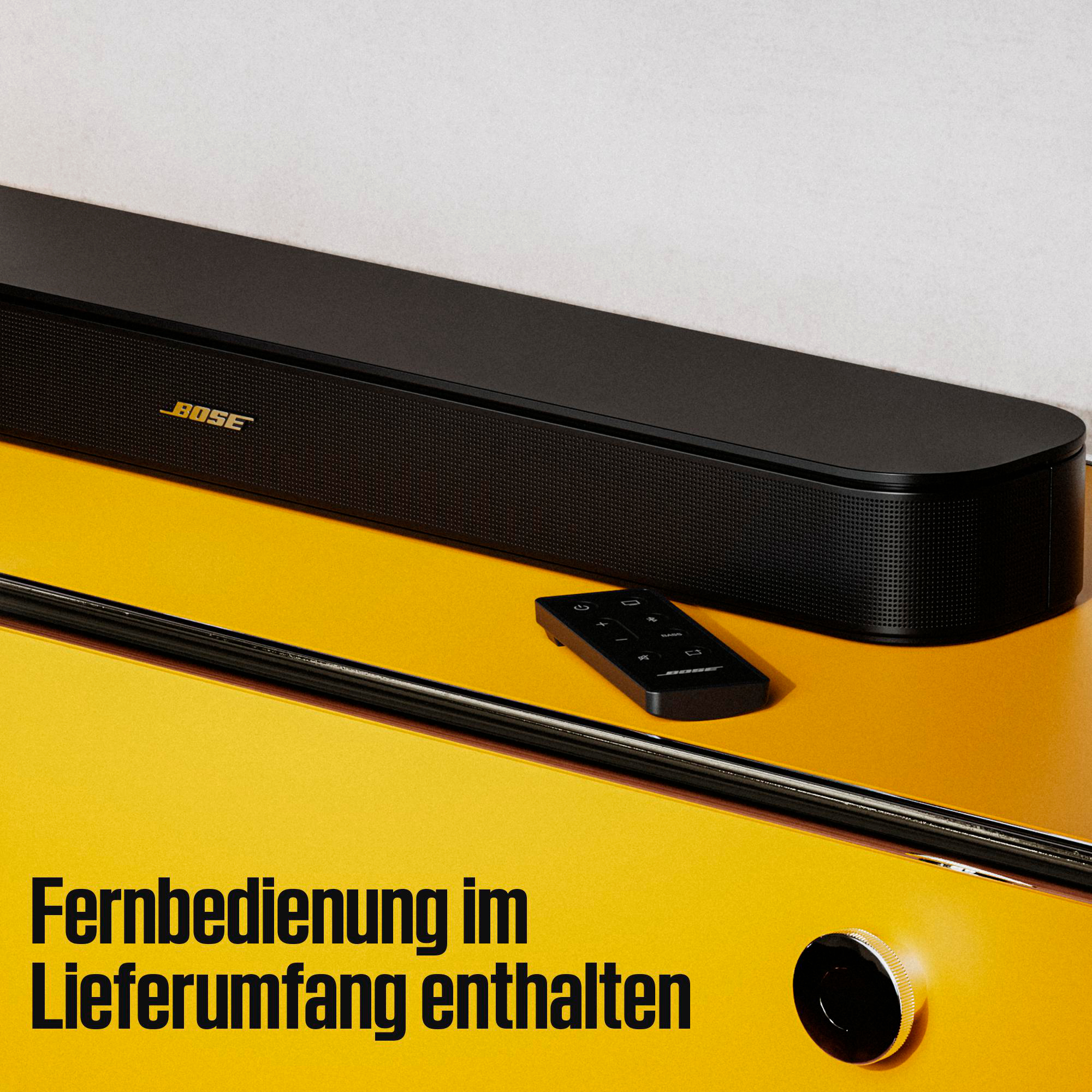 Schwarze Bose Soundbar und kleine Fernbedienung auf gelber Oberfläche mit Text Fernbedienung im Lieferumfang enthalten.