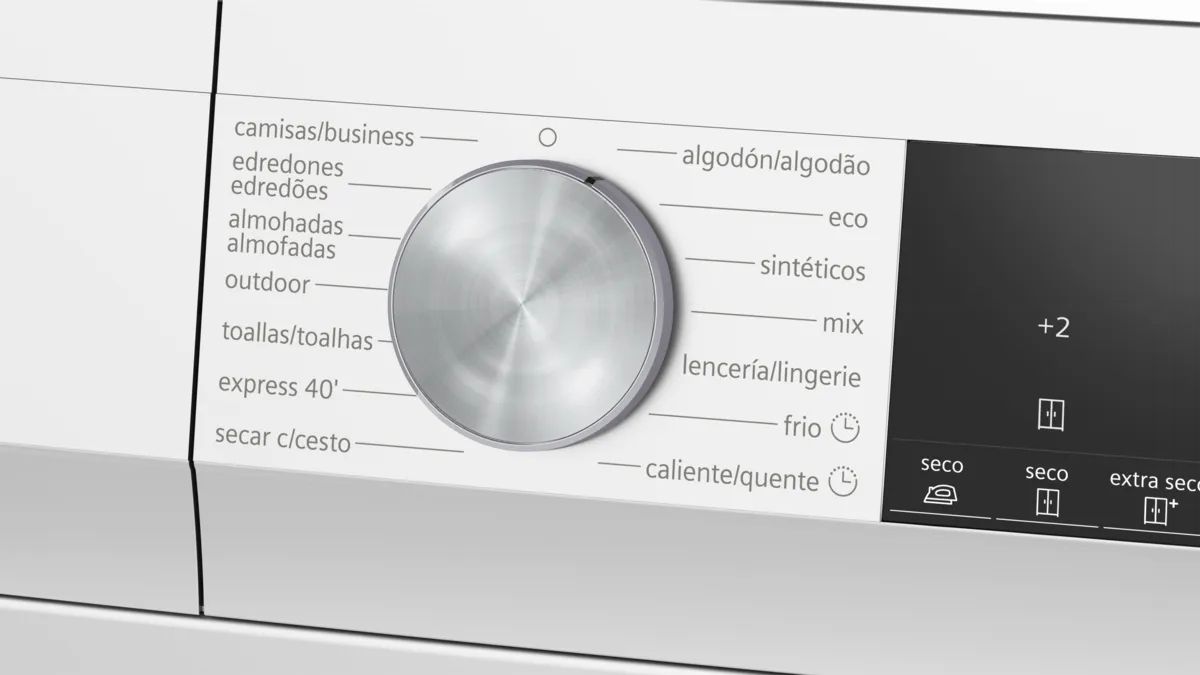 Primer plano de un selector de programas plateado en una lavadora blanca con varios programas.