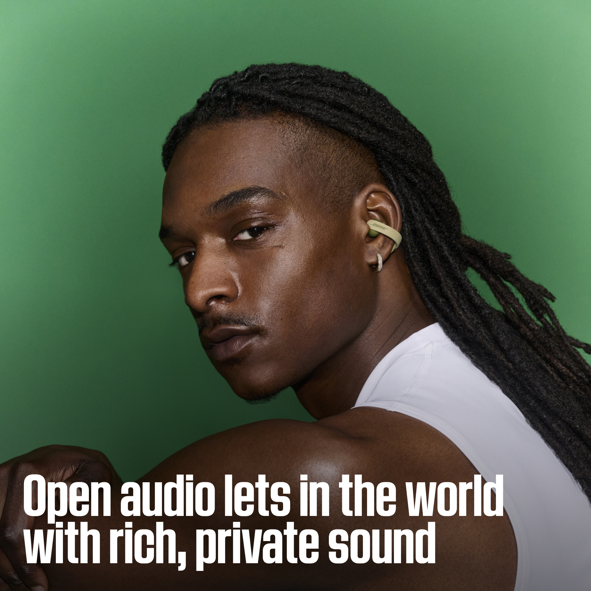 Un homme avec des dreadlocks portant des écouteurs verts devant un fond vert.