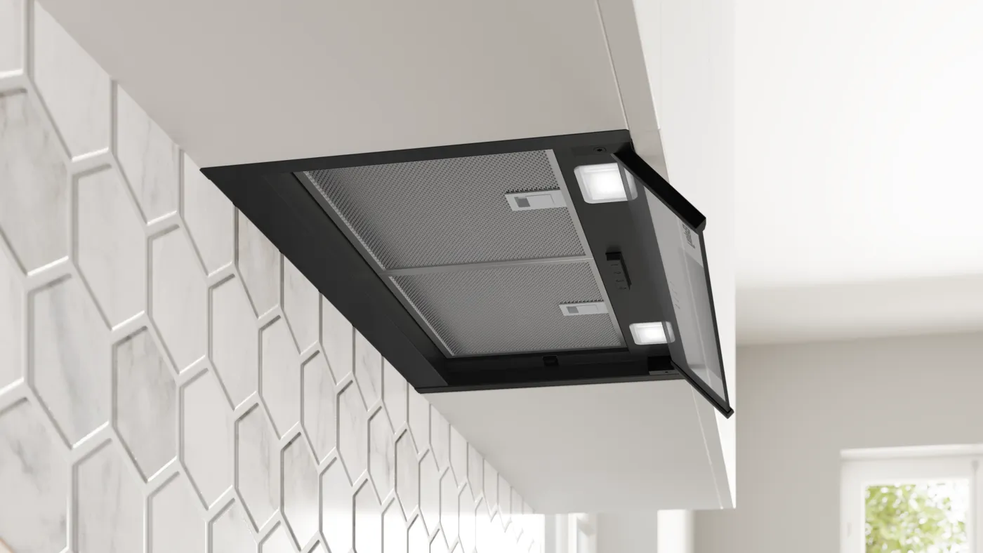 Una campana extractora negra con luces integradas y filtros metálicos está montada bajo un armario de cocina superior.