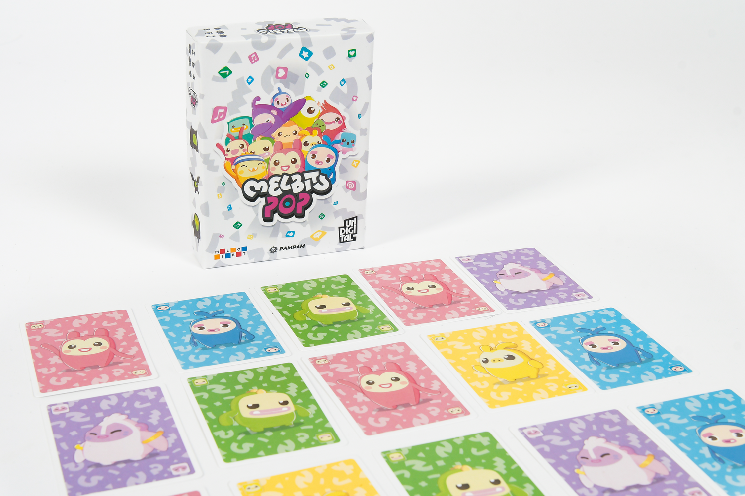 Caja del juego Melbits Pop con personajes coloridos y cartas dispuestas sobre una mesa blanca.
