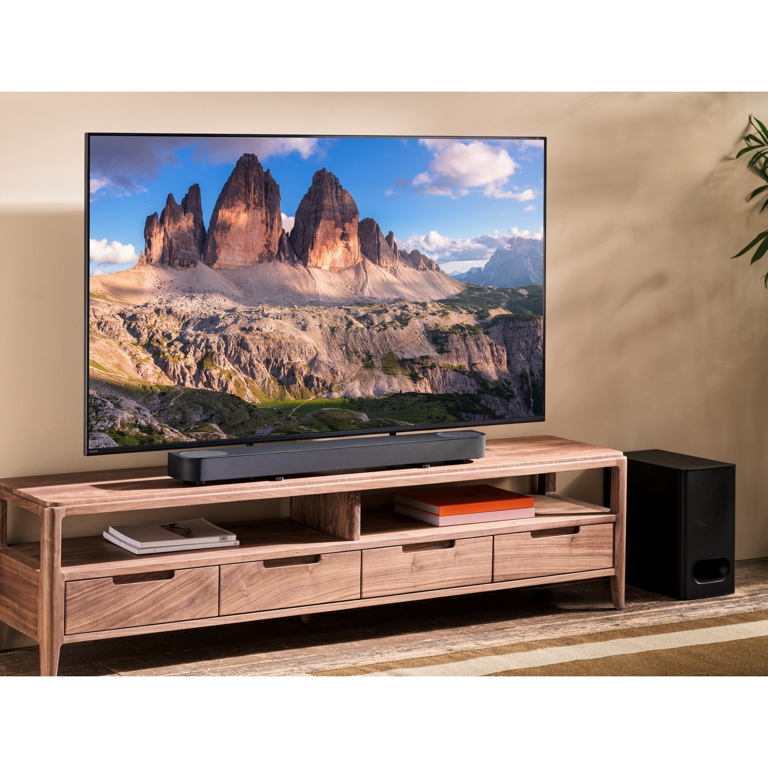 Un téléviseur avec paysage de montagne sur un meuble en bois avec barre de son et subwoofer dans une pièce.