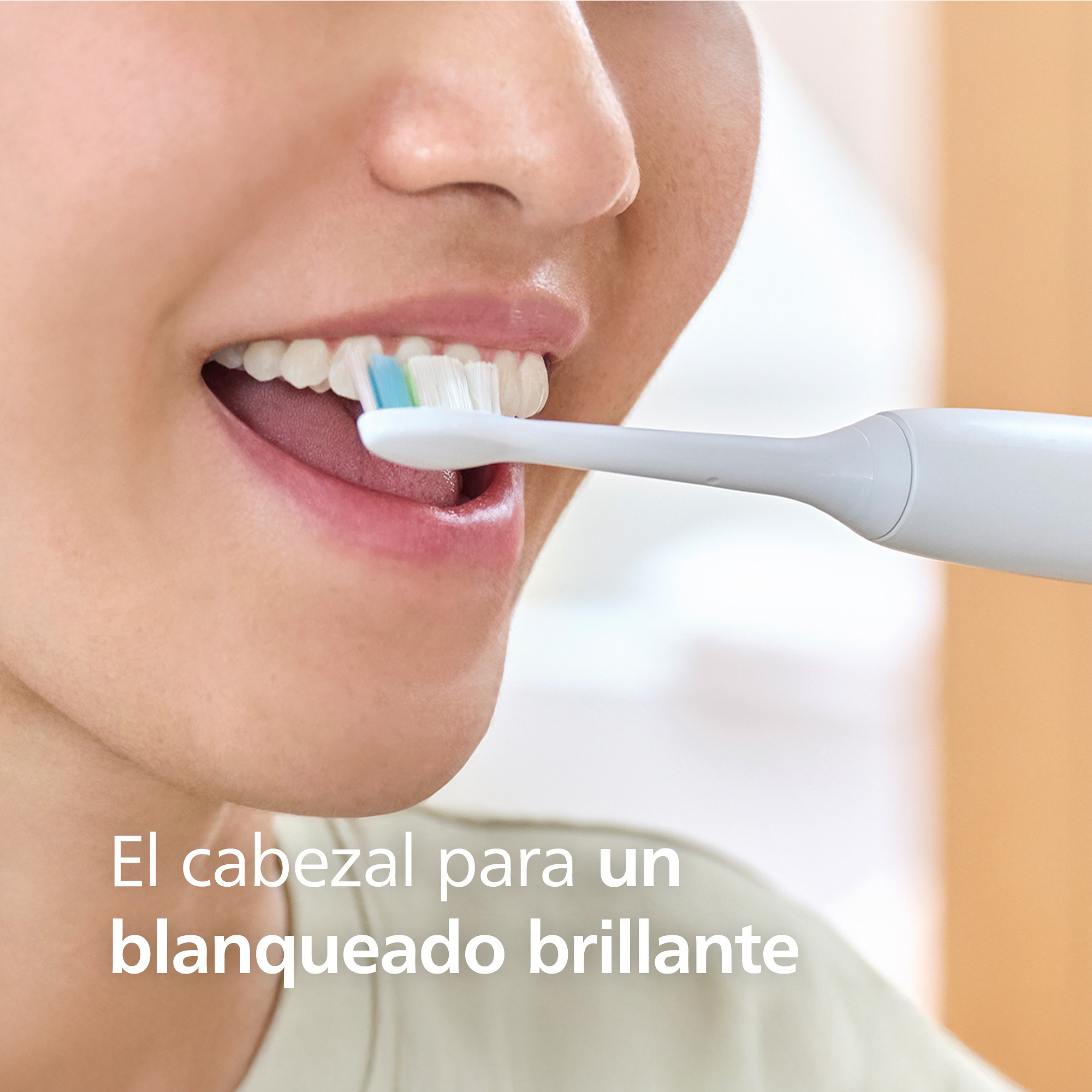 Una persona cepillándose los dientes blancos con un cepillo eléctrico blanco en una habitación luminosa.
