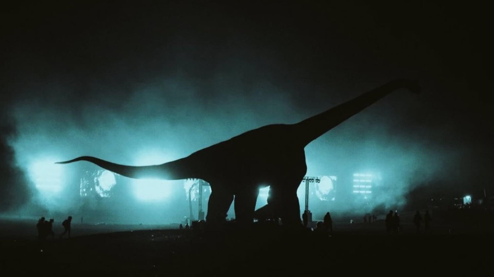 Die dunkle Silhouette eines riesigen Dinosauriers leuchtet vor hellem, bläulichem Nebel im Hintergrund auf.