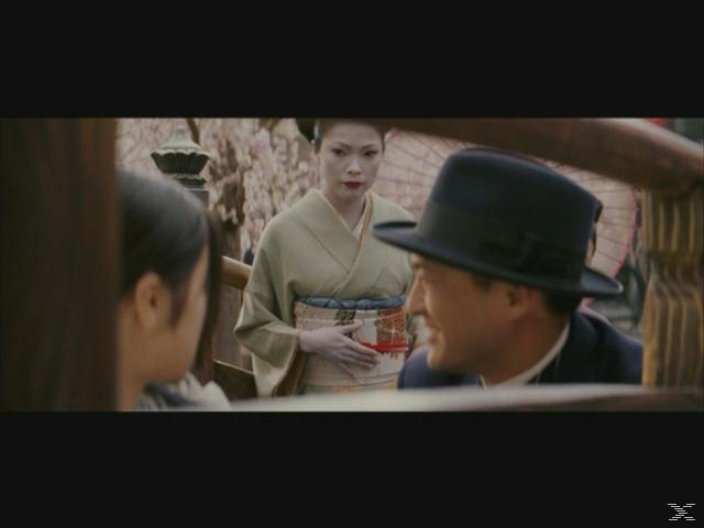 Eine Frau im Kimono und ein Mann mit Hut unterhalten sich im Freien.