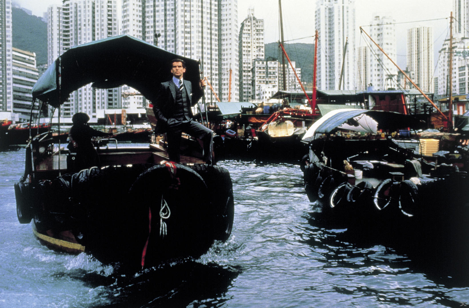 Ein Mann im Anzug steht auf einem Boot vor einer Skyline in Hongkong.