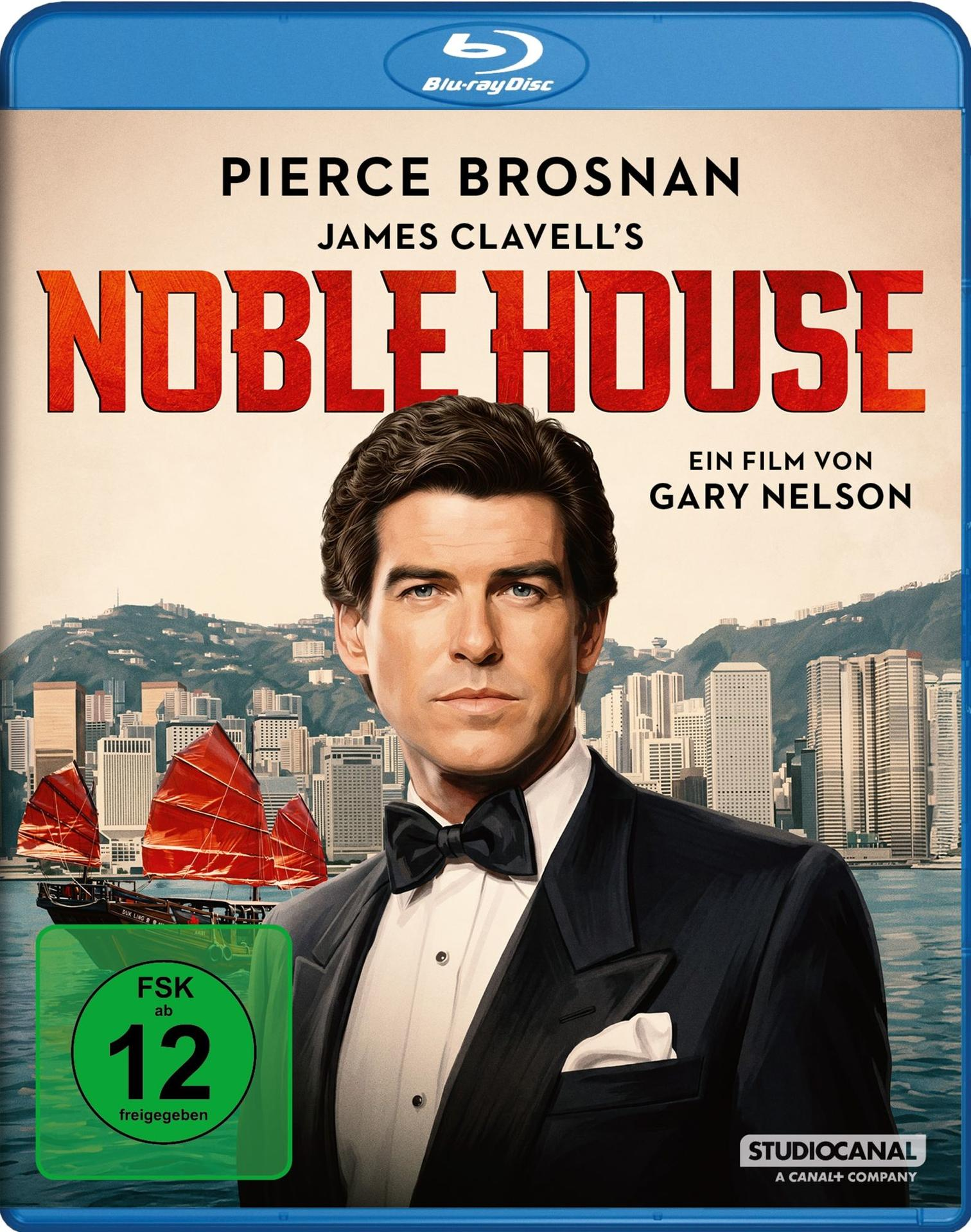 Blu-ray-Cover von Noble House mit Pierce Brosnan in einem Tuxedo vor einer Skyline von Hongkong und Segelbooten.