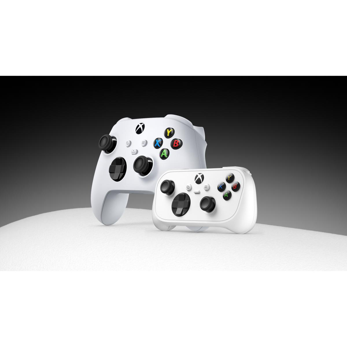 Zwei weiße Xbox-Controller stehen auf einer weißen Oberfläche vor dunklem Hintergrund.