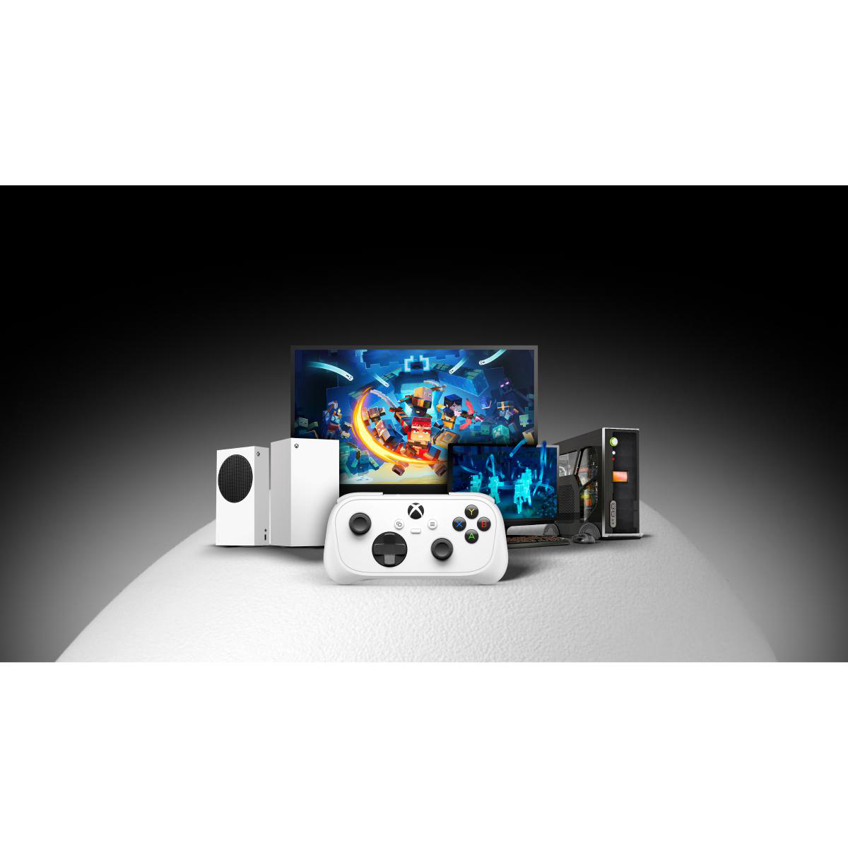 Eine weiße Xbox Series S Konsole, ein Controller, ein Monitor und ein PC auf einem Tisch vor schwarzem Hintergrund.