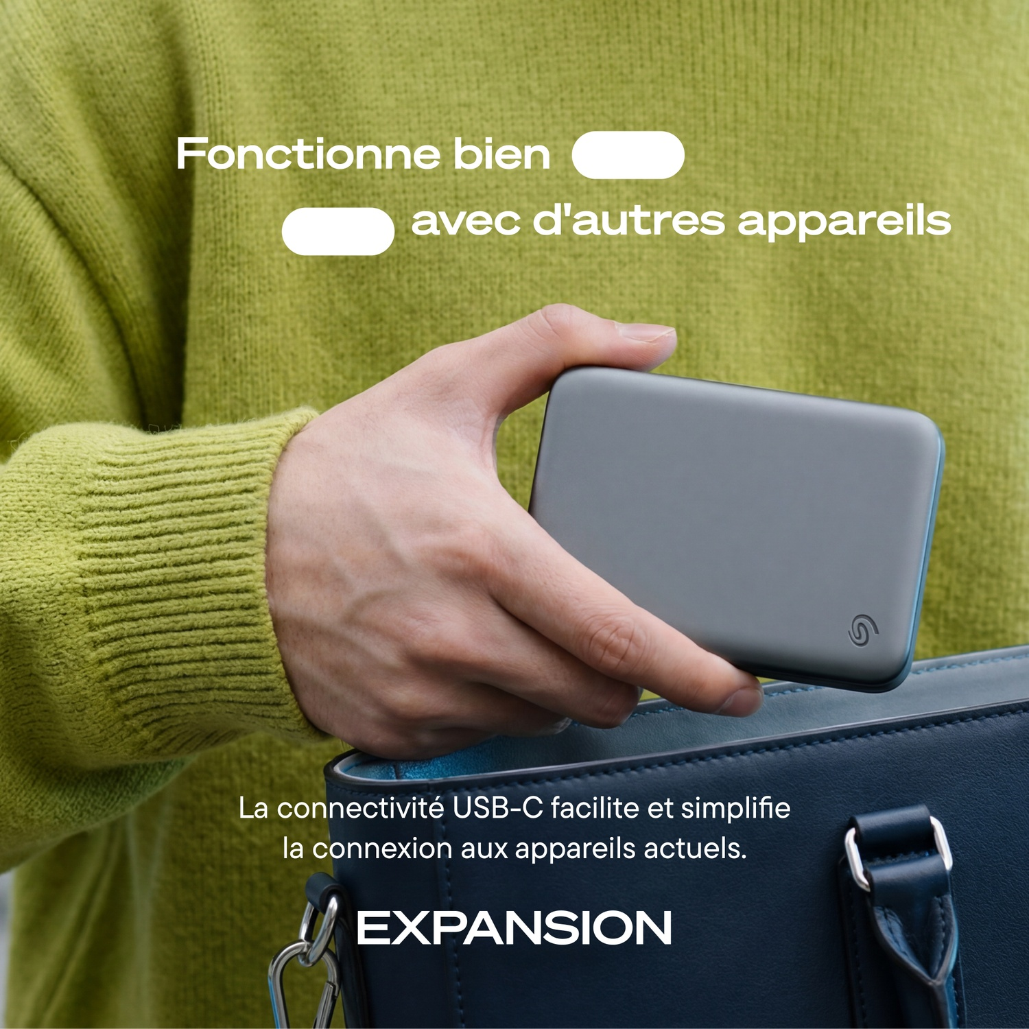 Une personne en pull vert place un disque dur externe dans un sac bleu.