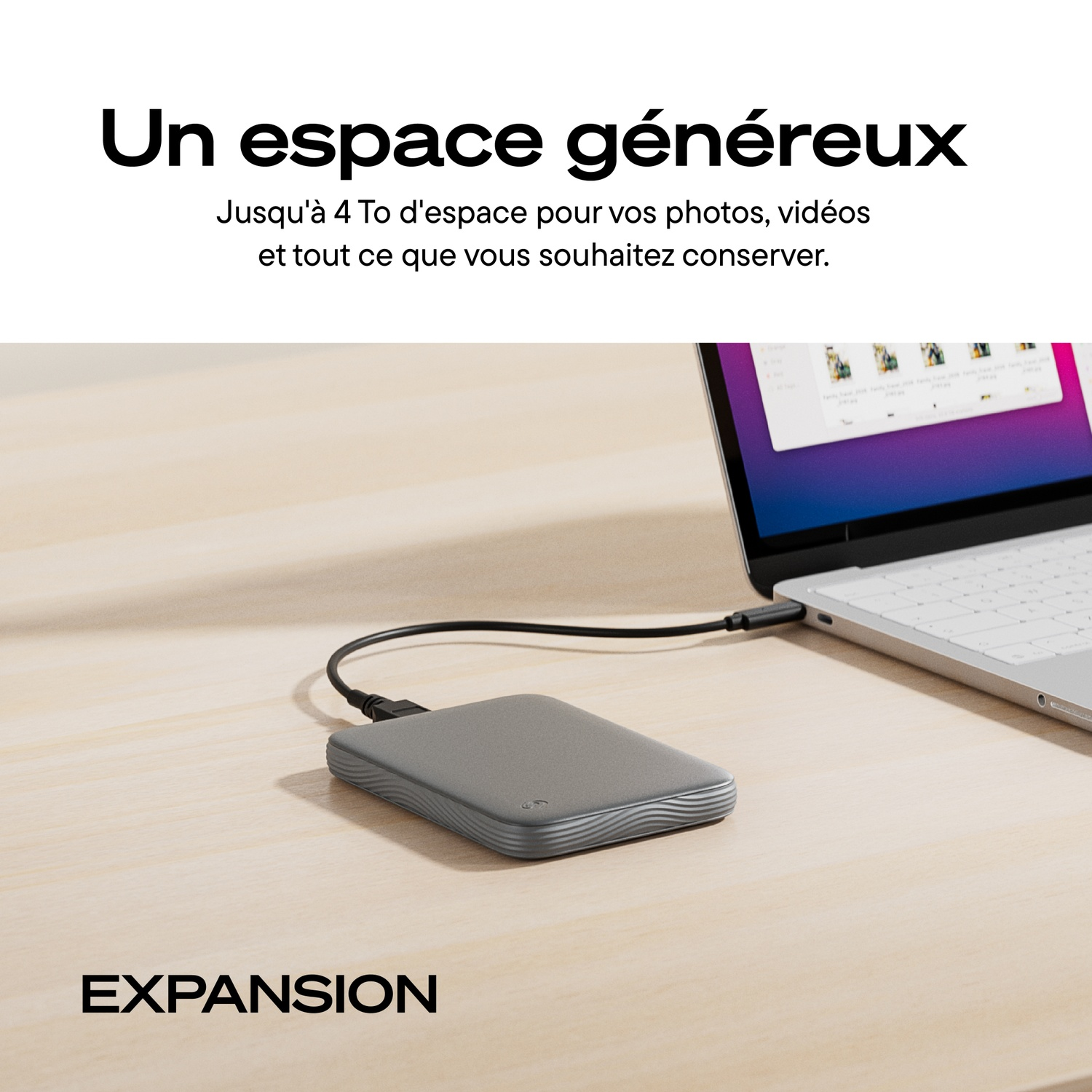 Un disque dur externe gris est relié par un câble à un ordinateur portable sur un bureau en bois.